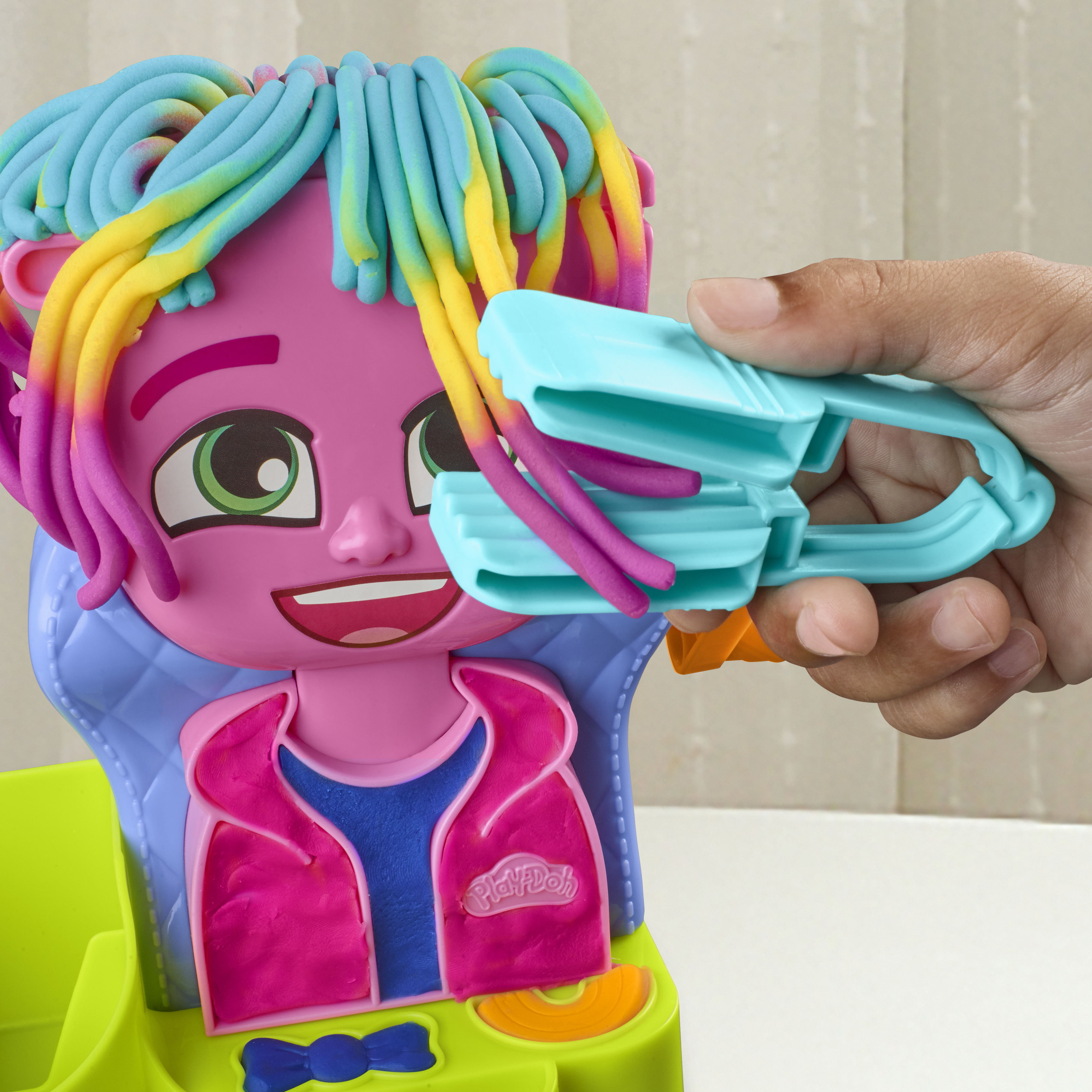 Un juguete Play-Doh rosa con pelo colorido está siendo peinado con una herramienta de plástico azul.