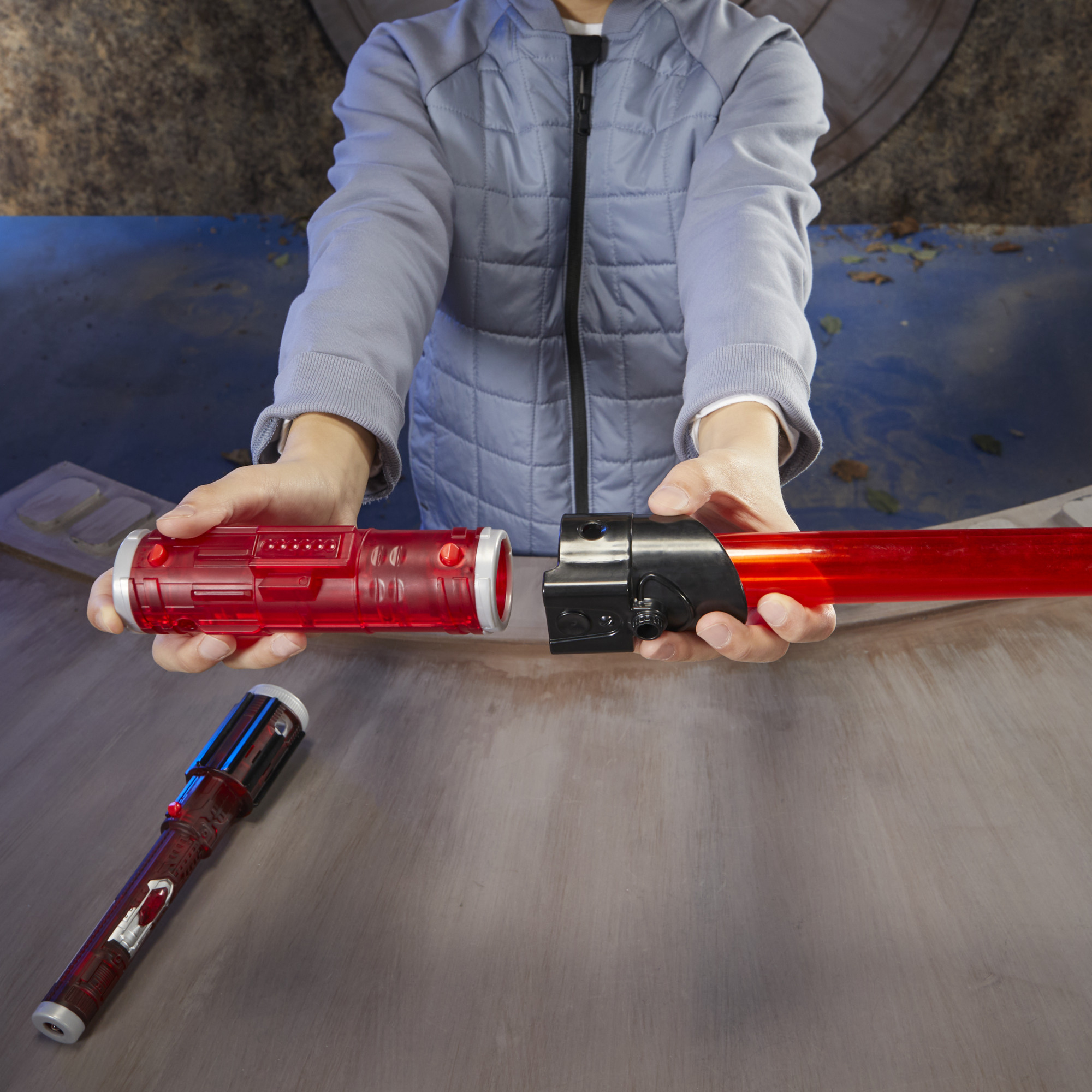 Osoba składająca czerwoną zabawkę miecza świetlnego. Rękojeść jest czarna, a ostrze czerwone. Na stole jest inny miecz świetlny.