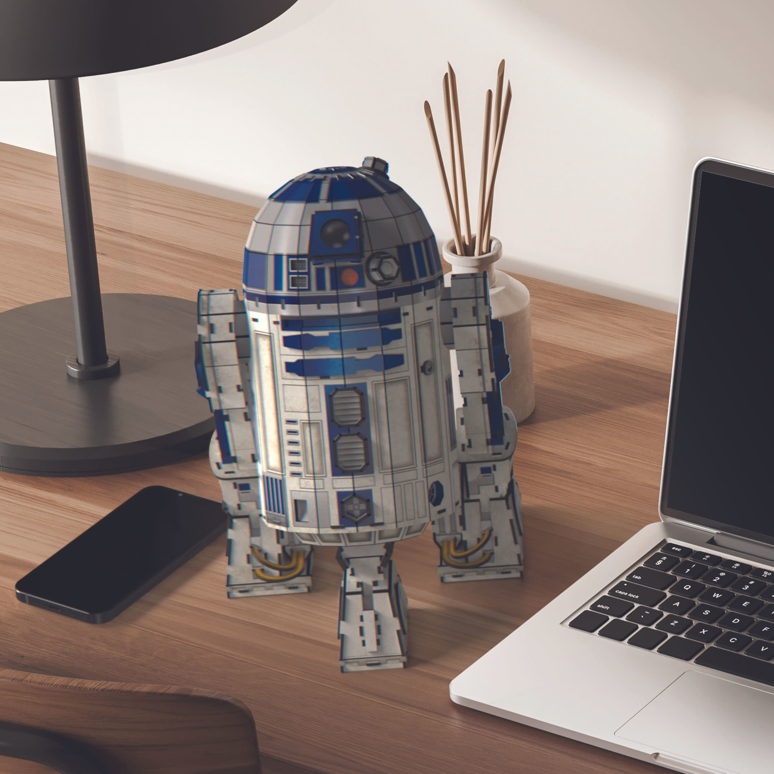 Model R2-D2, laptop, telefon i lampa stoją na drewnianym biurku. Patyczki do kadzideł są w wazonie.