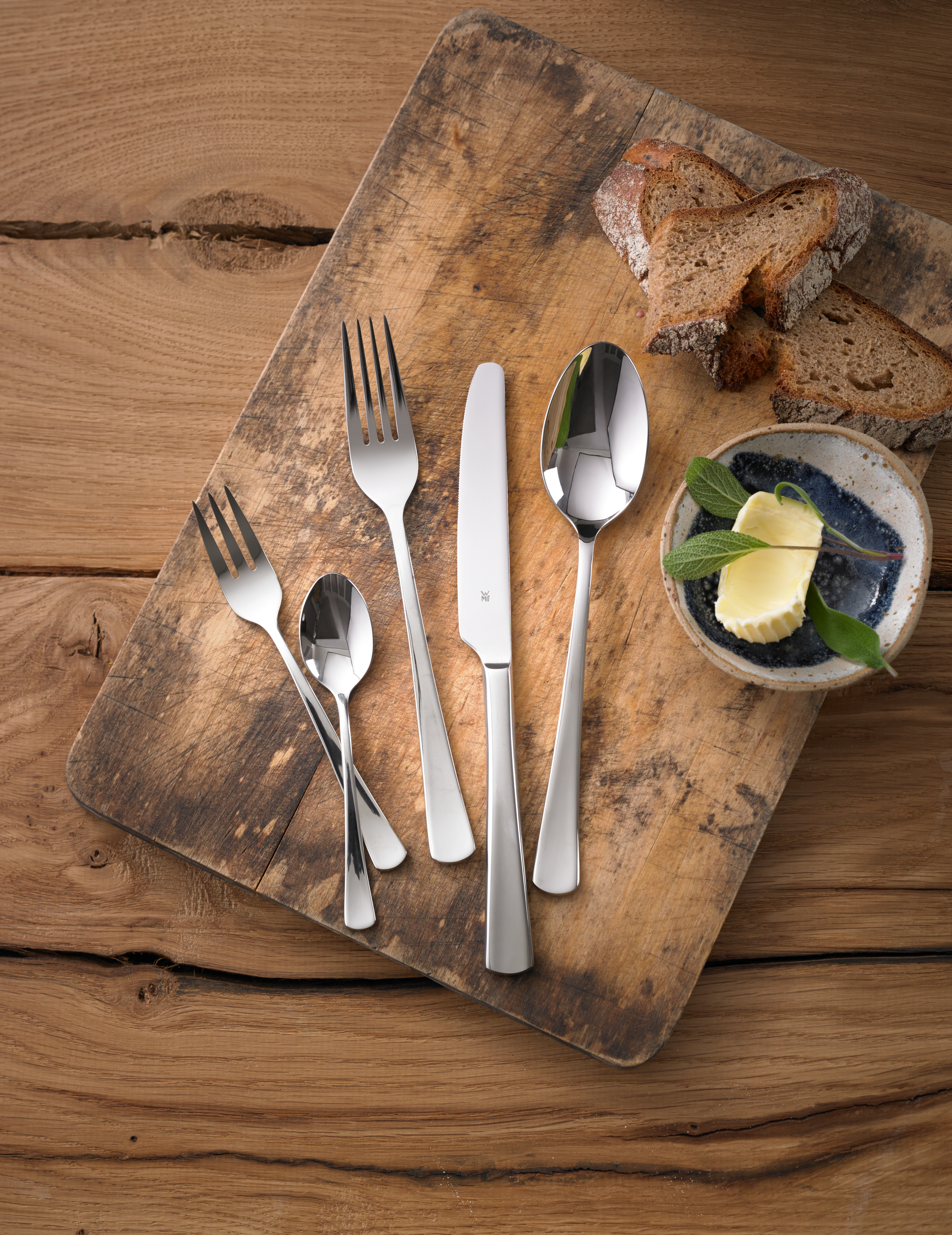 Rustykalna drewniana deska ze sztućcami, chlebem i masłem. Scena rozgrywa się na drewnianym stole.