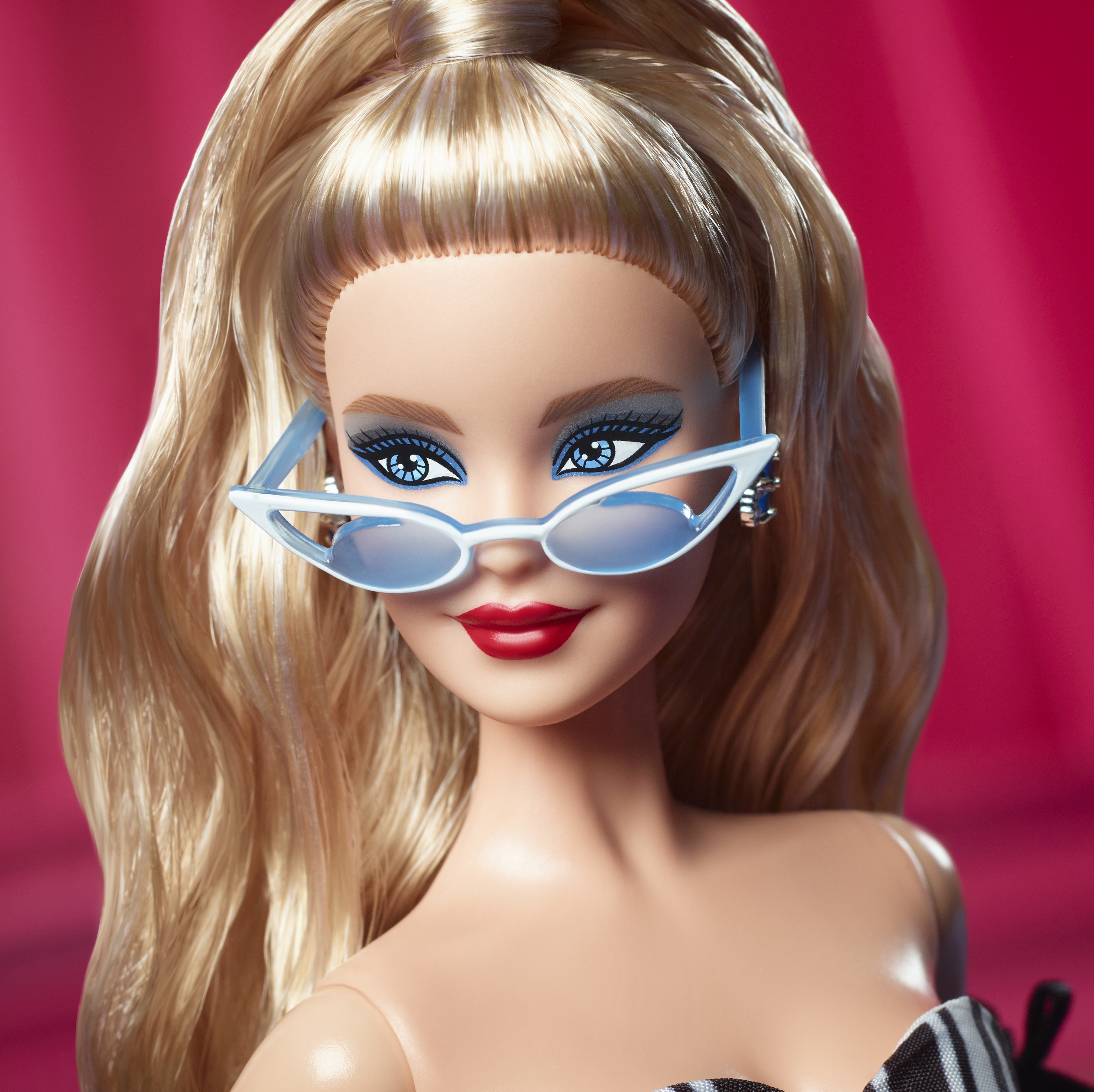 Primer plano de una muñeca Barbie con cabello rubio, ojos azules y gafas de sol. Tiene lápiz labial rojo y una blusa en blanco y negro.