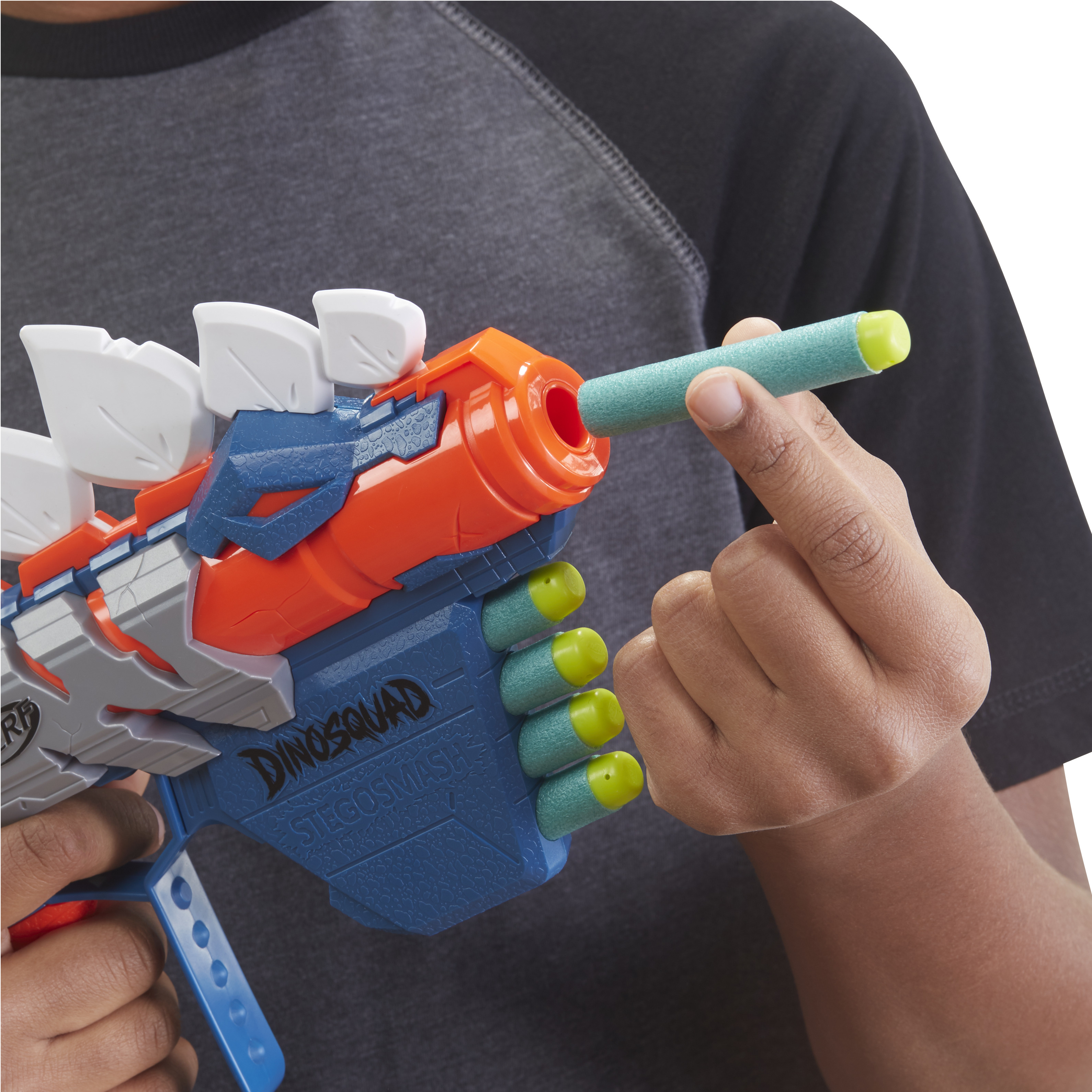 Eine Person lädt eine blaue, orangefarbene und weiße Spielzeugpistole mit einem grünen Pfeil. Die Waffe hat weiße Flossen und gelbe Spitzen.