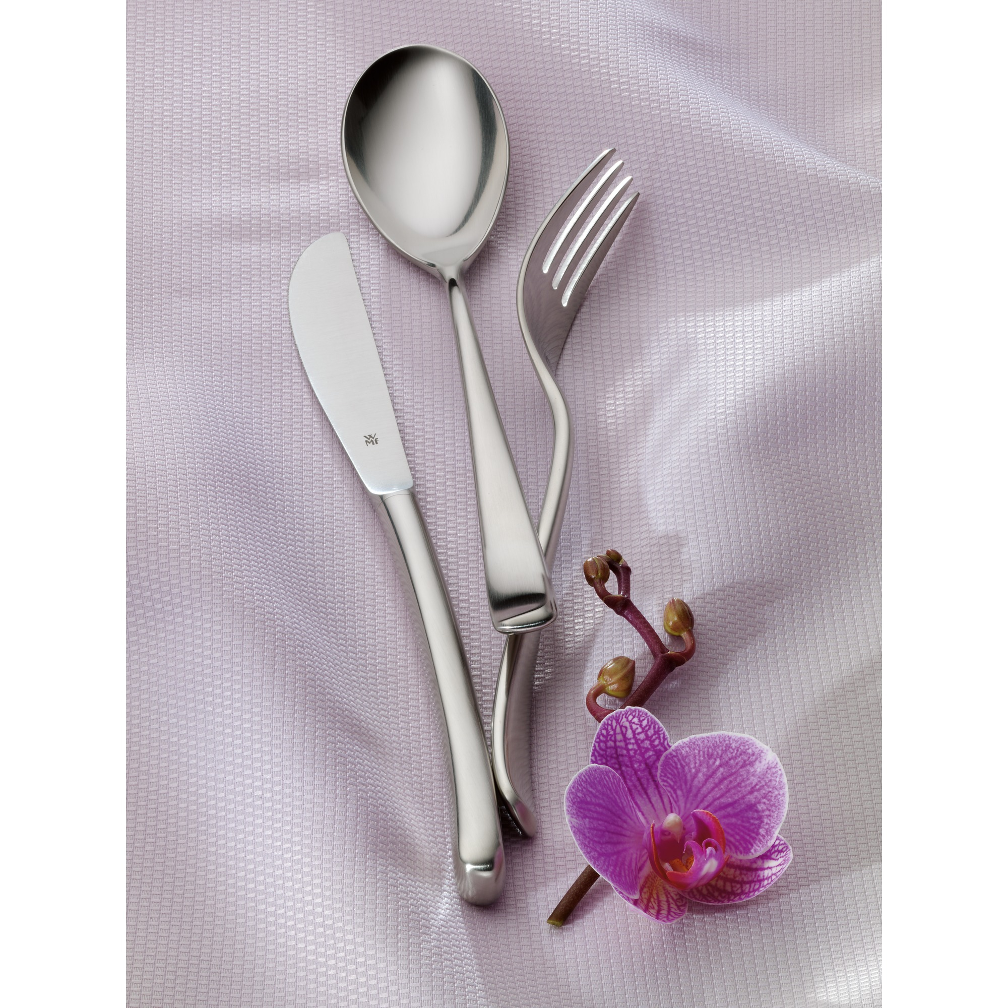 Ein Messer, ein Löffel und eine Gabel liegen auf einem lilafarbenen, strukturierten Stoff, begleitet von einer lila Orchidee.