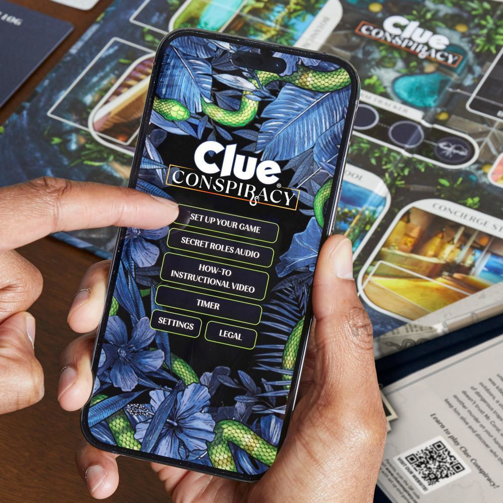 Eine Hand hält ein Telefon, auf dem die App 'Clue Conspiracy' angezeigt wird. Der Bildschirm zeigt Menüoptionen wie 'Spiel einrichten' und 'Anleitungsvideo'.