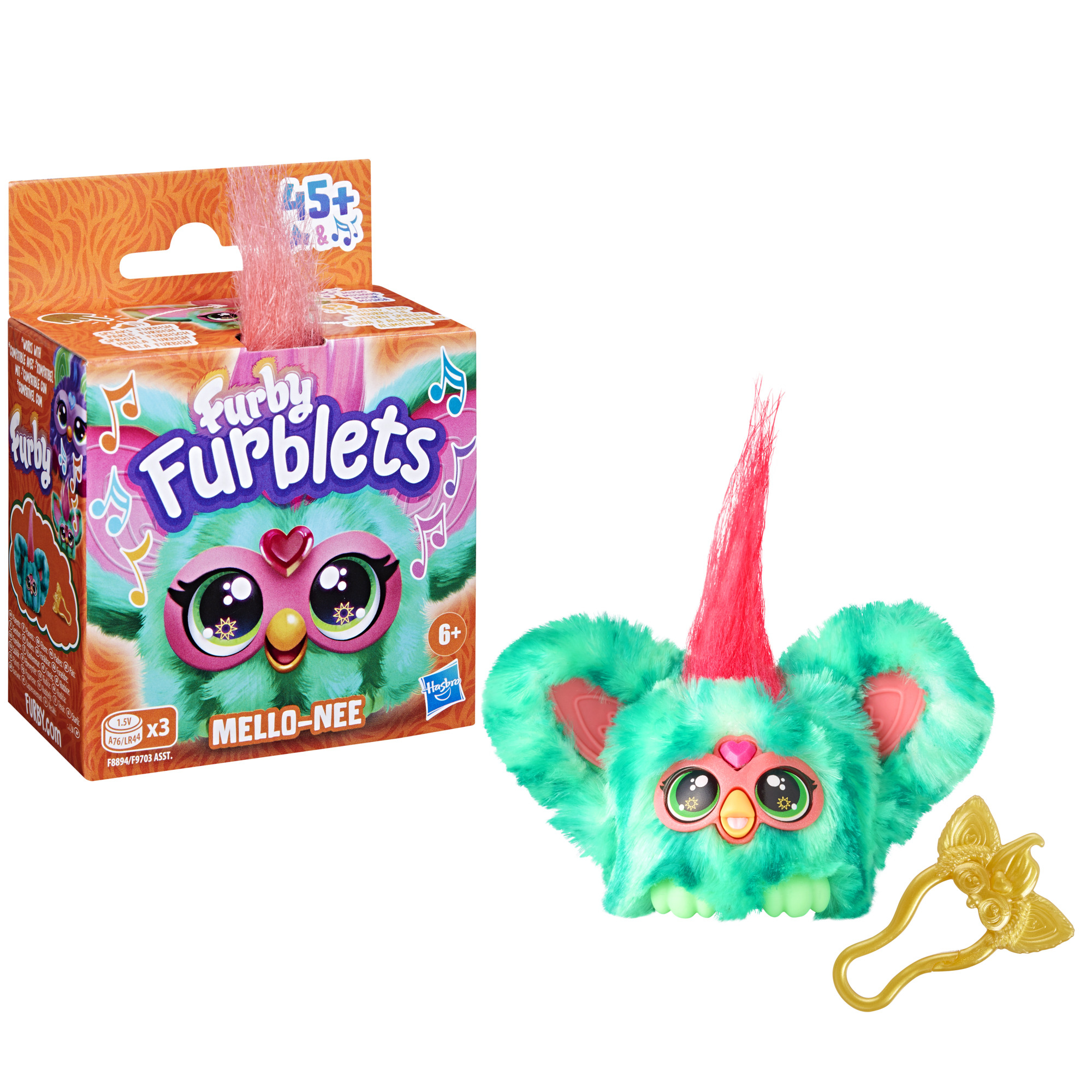 Un juguete Furblets con pelaje verde azulado, detalles rosas y una cresta roja. La caja es naranja y hay un accesorio dorado al lado.