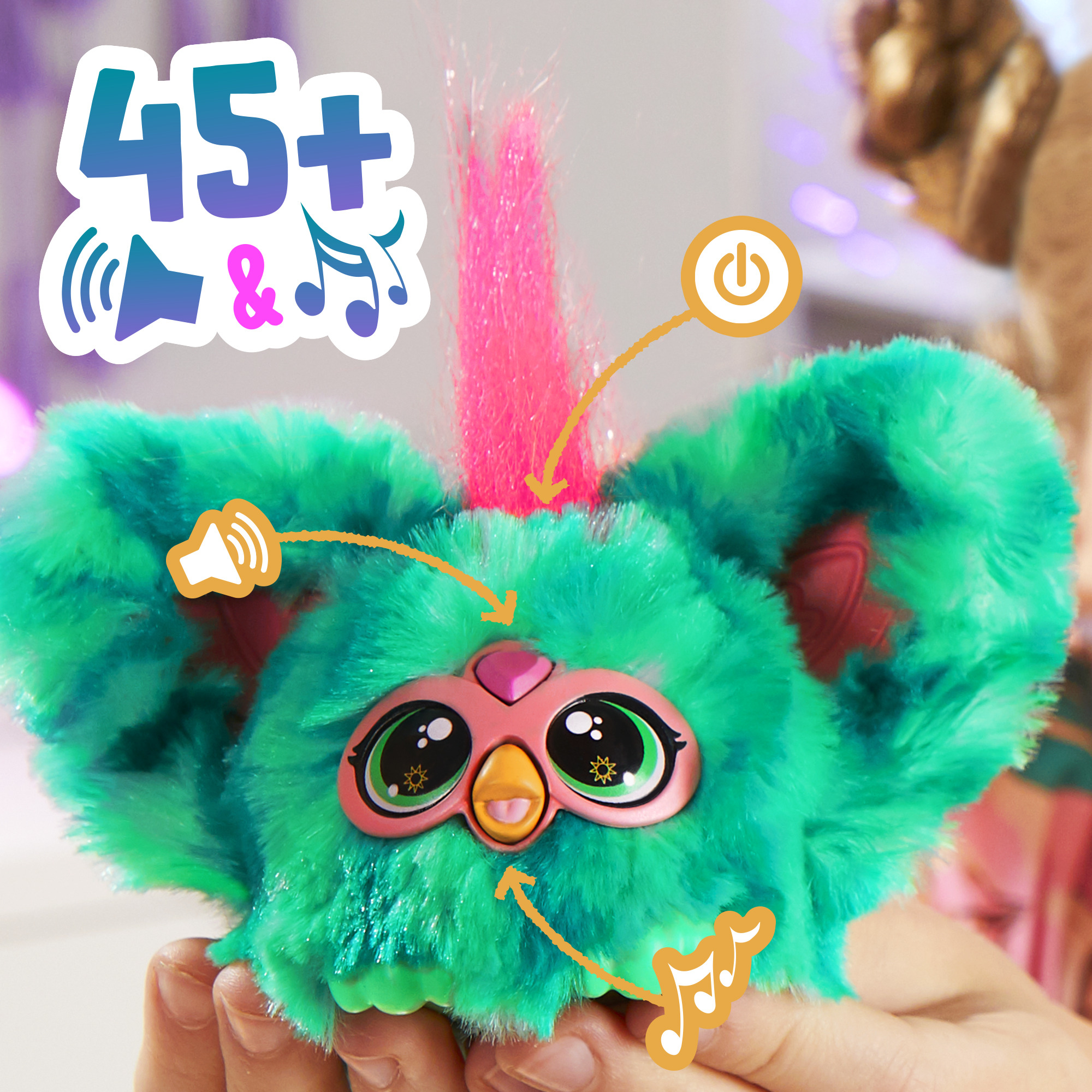 Un juguete Furby verde y rosa se sostiene en las manos. Tiene ojos grandes, una cara rosa y un mechón de pelo rosa. Tiene iconos de sonido y música.