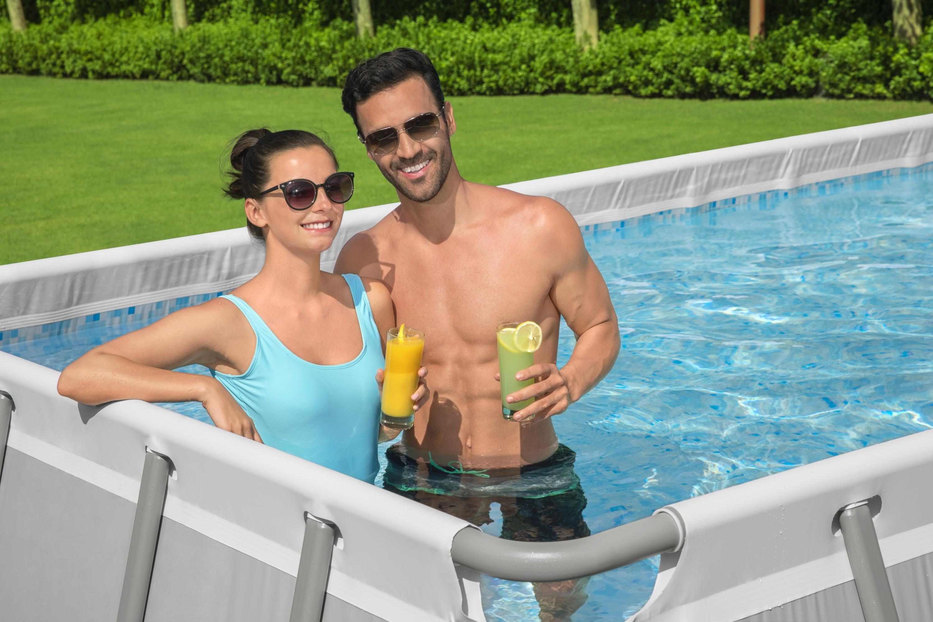 Para w basenie z napojami. Zielony trawnik i krzewy w tle.