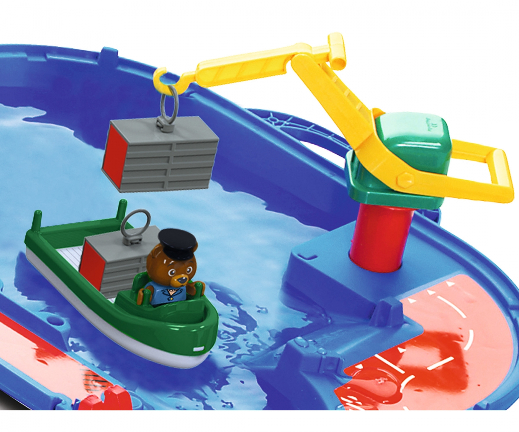 Eine Spielzeugbootszene mit einer Bärenfigur in einem grünen Boot. Ein Kran hebt einen Container an. Blaues Wasser und ein roter Weg sind sichtbar.