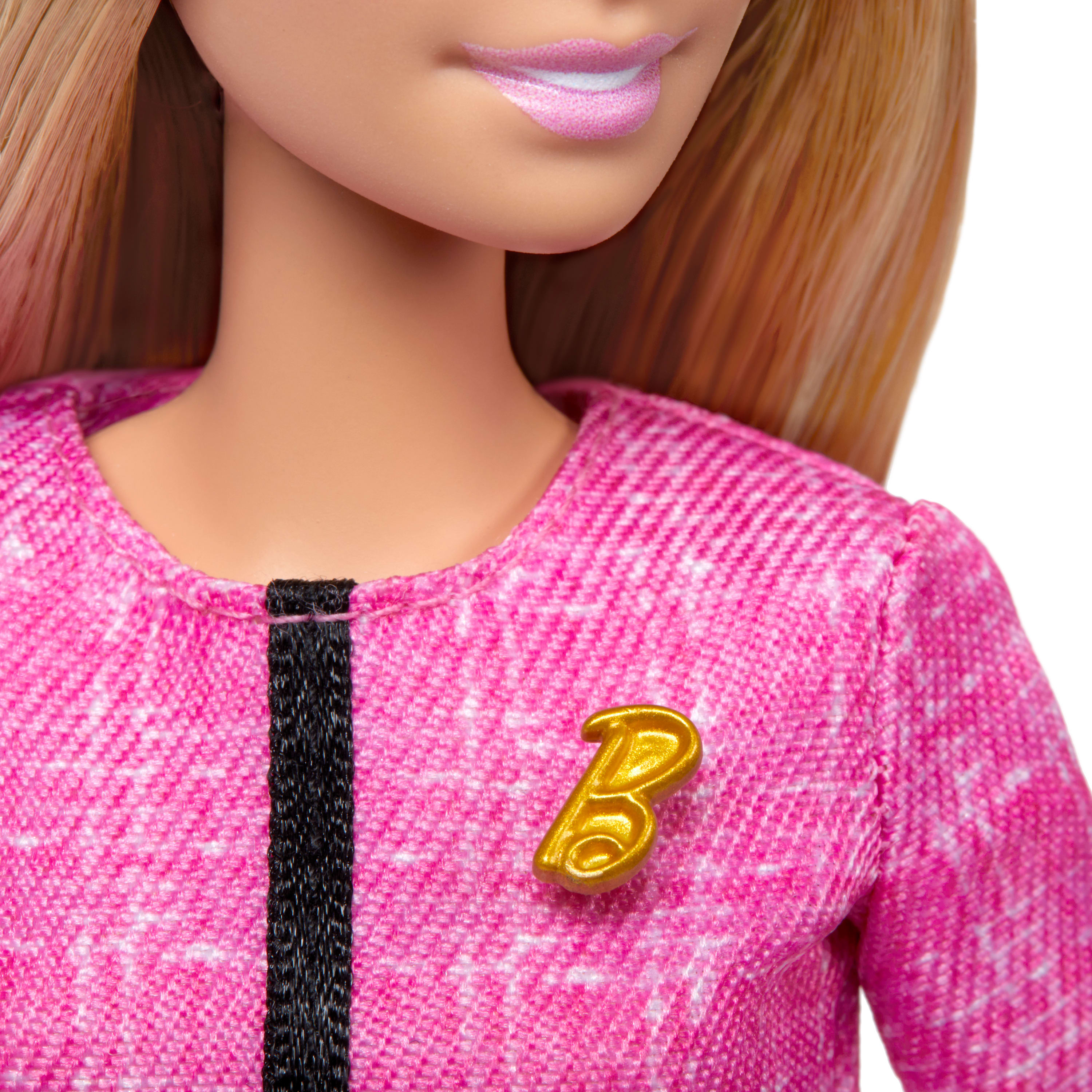 Nahaufnahme von Puppengesicht und rosa Outfit. Das Outfit hat eine goldene 'B'-Anstecknadel.