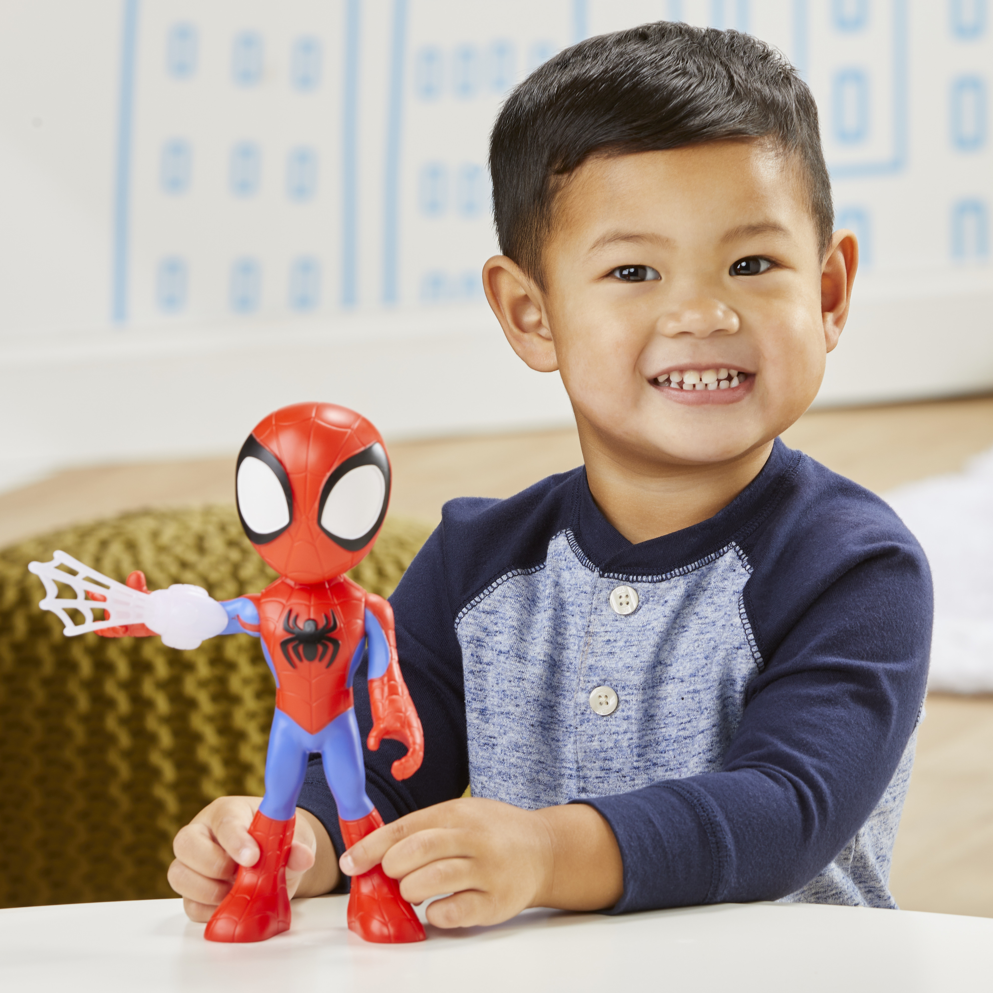 Un niño sonriente sostiene un juguete de Spider-Man. El juguete es rojo, azul y blanco. El niño lleva una camisa azul.
