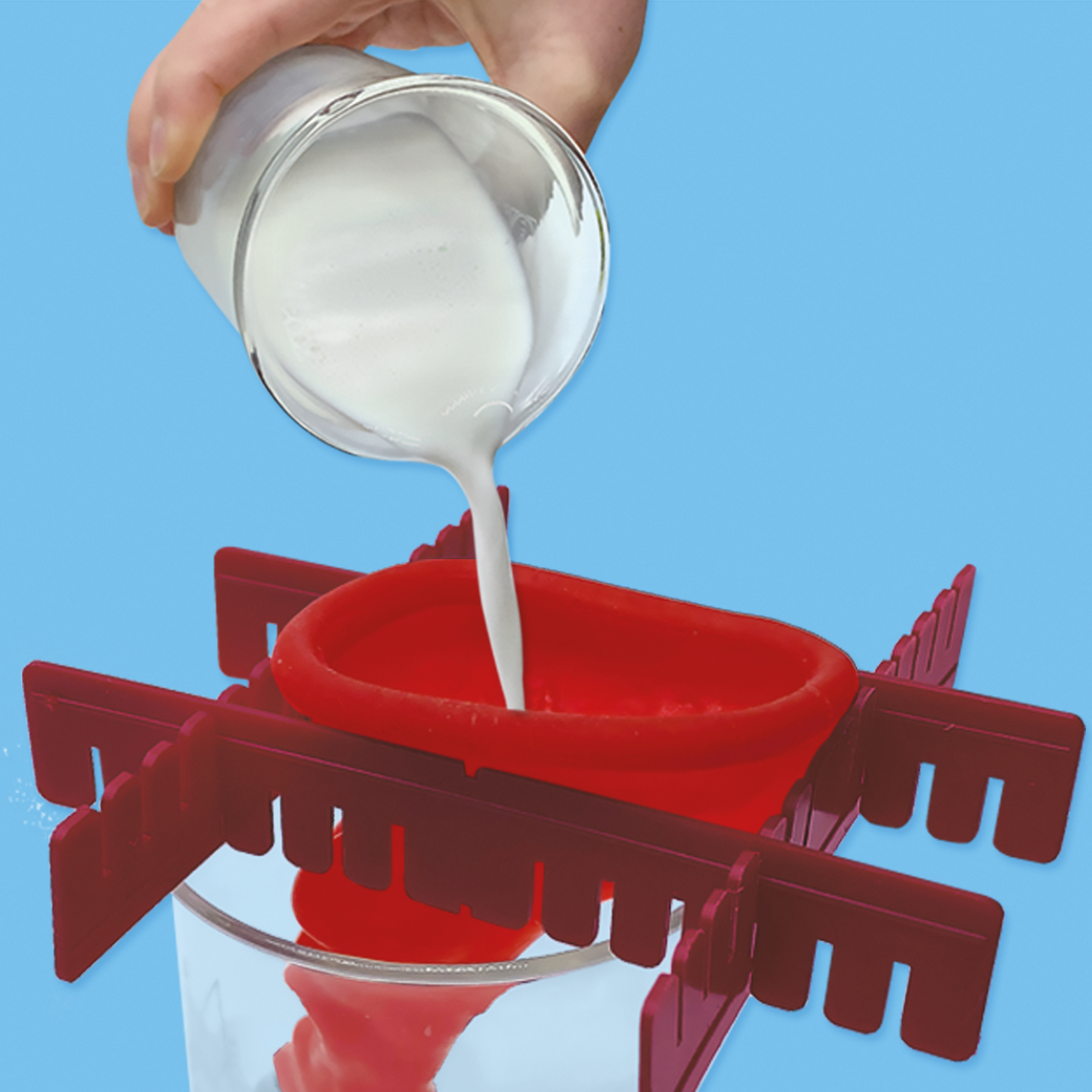 Ręka wlewa mleko ze szklanki do czerwonego lejka, a następnie do innej szklanki. Niebieskie tło.