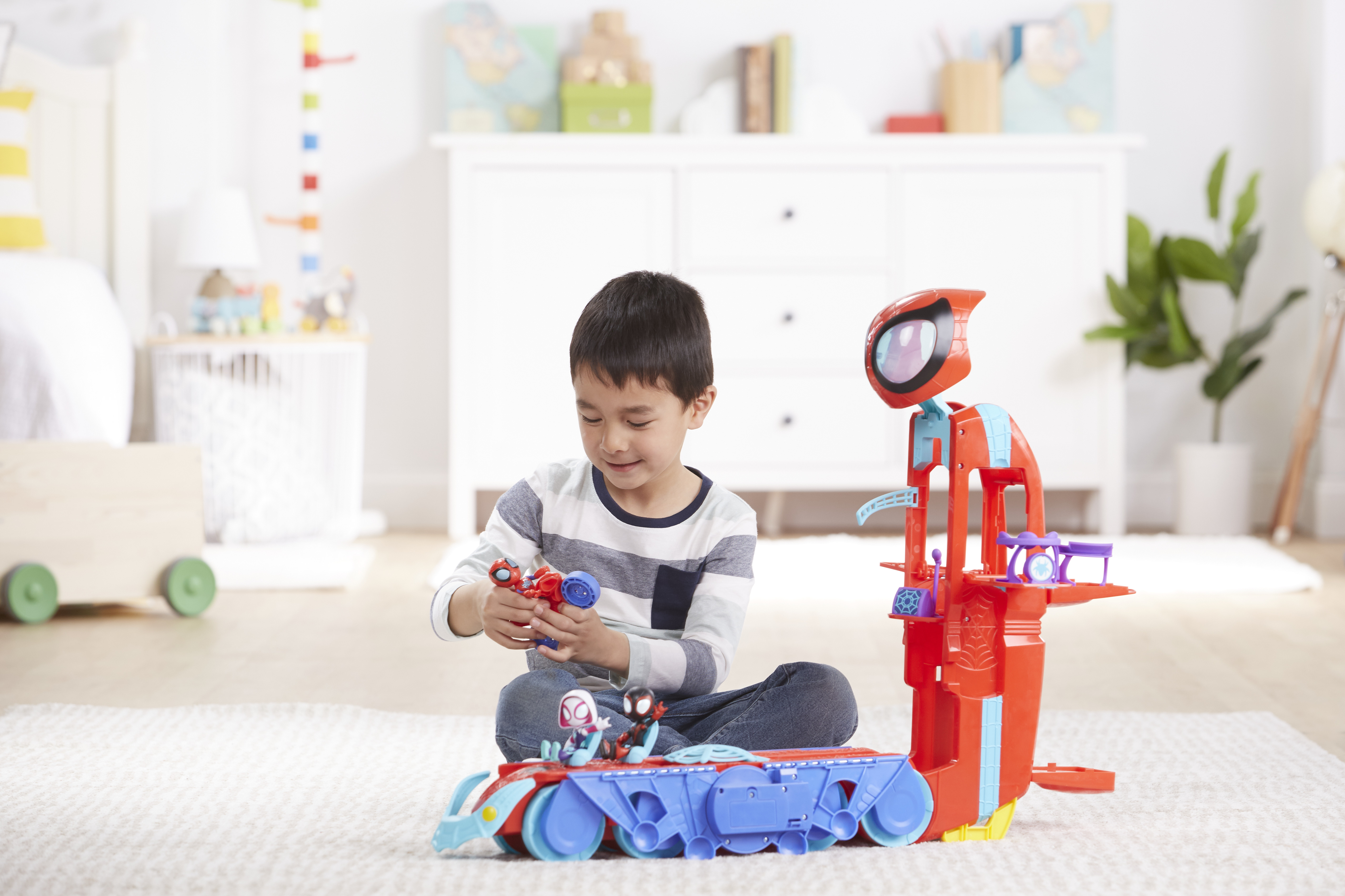 Chłopiec bawi się zabawkami Spider-Mana. Czerwono-niebieski zestaw do zabawy i figurki w białym pokoju.