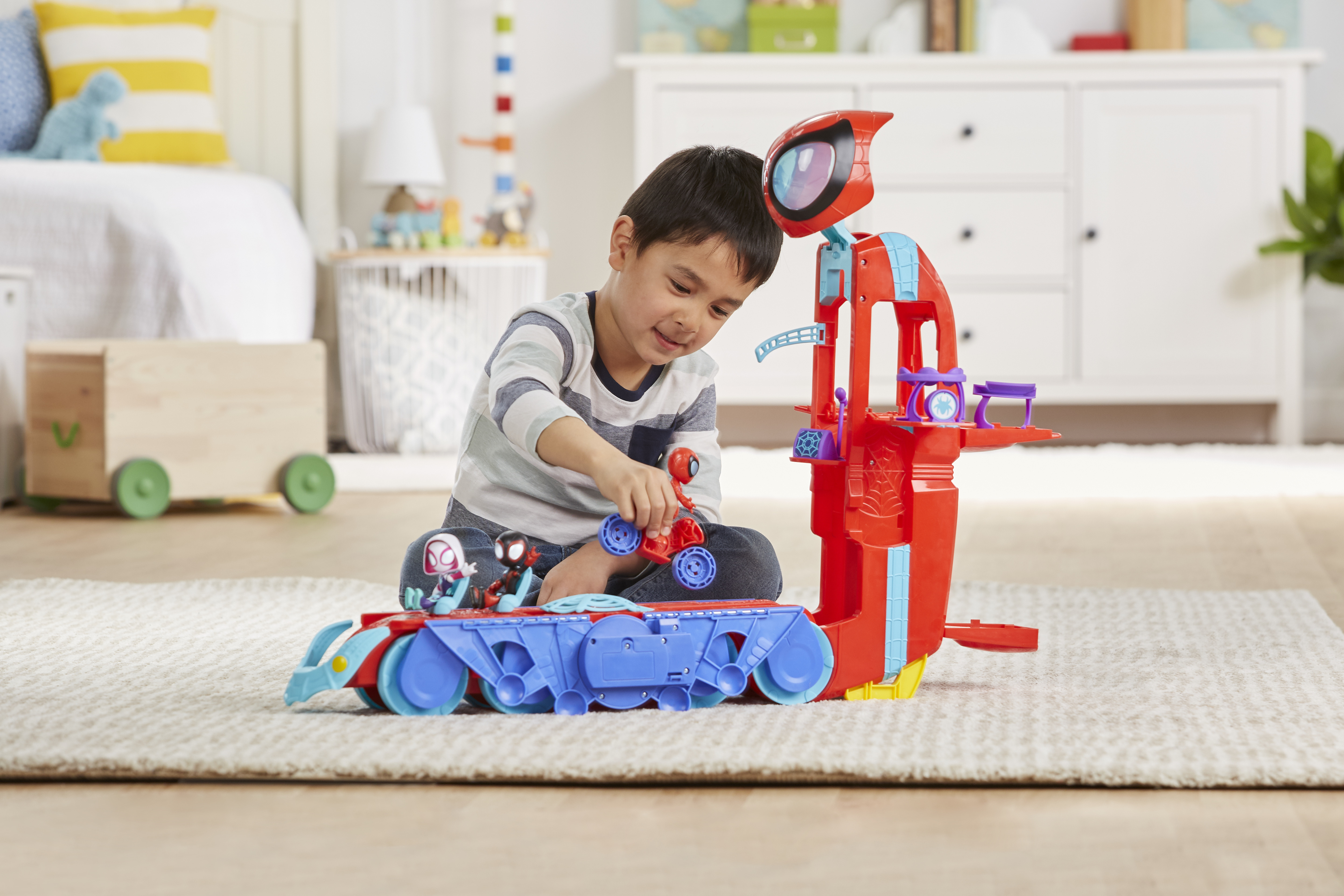 Chłopiec bawi się zestawem zabawek Spider-Man. Zawiera czerwoną wieżę, niebieski pojazd i figurki Spider-Mana.