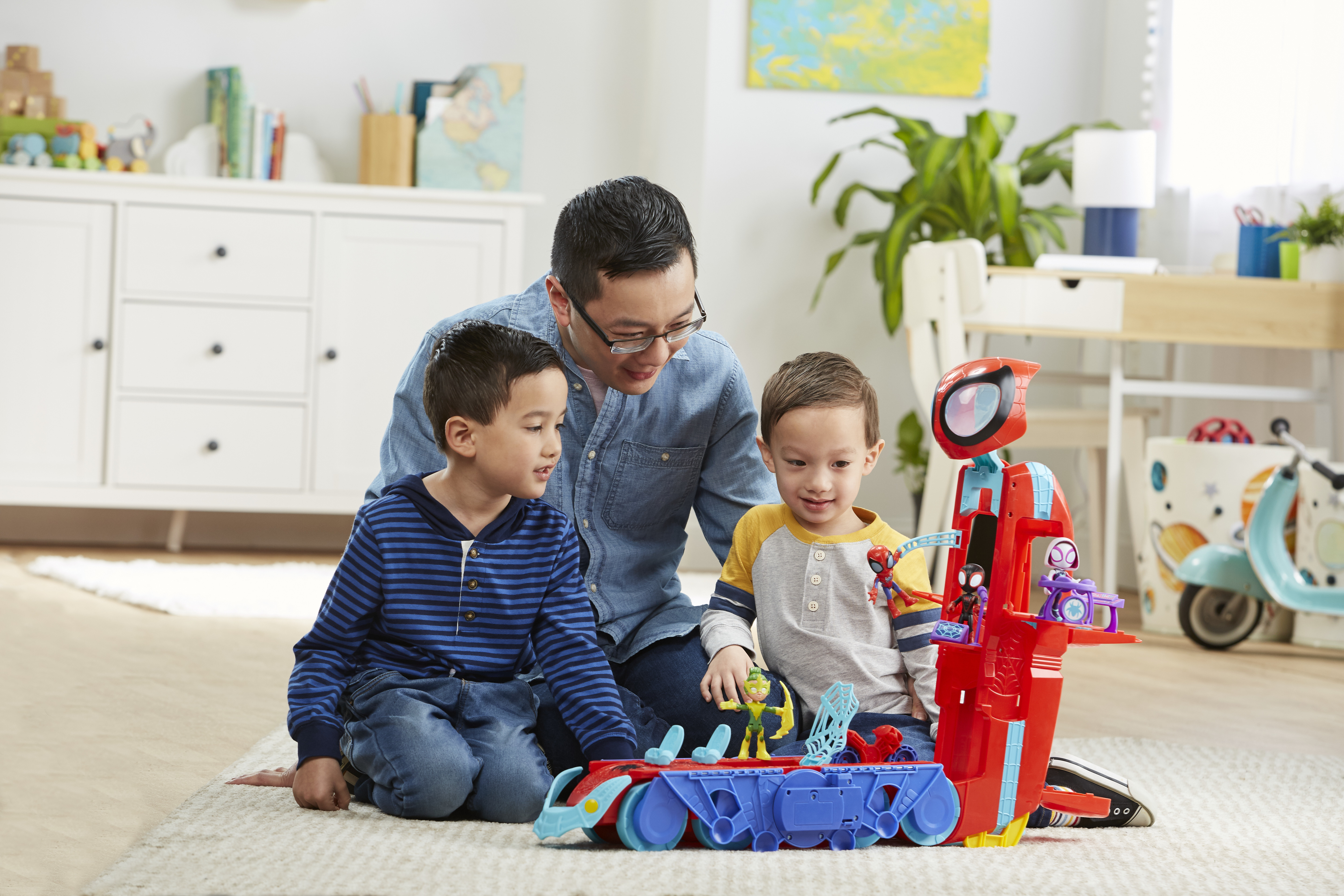 Mężczyzna i dwoje dzieci bawią się zestawem zabawek Spider-Man. Biała szafka i inne zabawki są w tle.