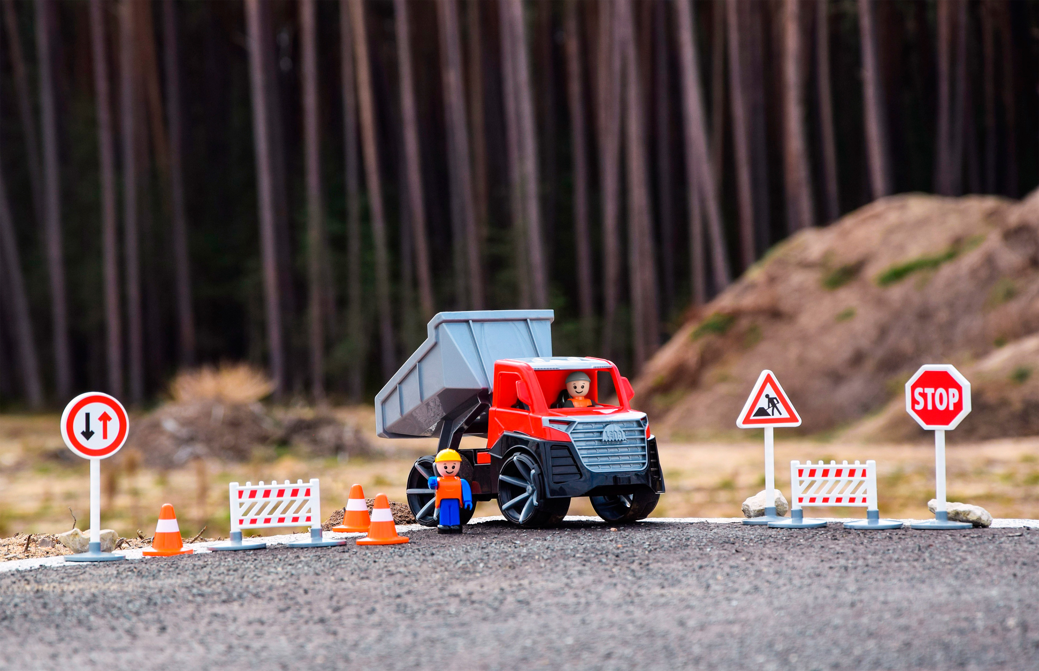 Zabawkowa scena budowy z ciężarówką, figurkami robotników, znakami drogowymi, pachołkami i tłem leśnym.