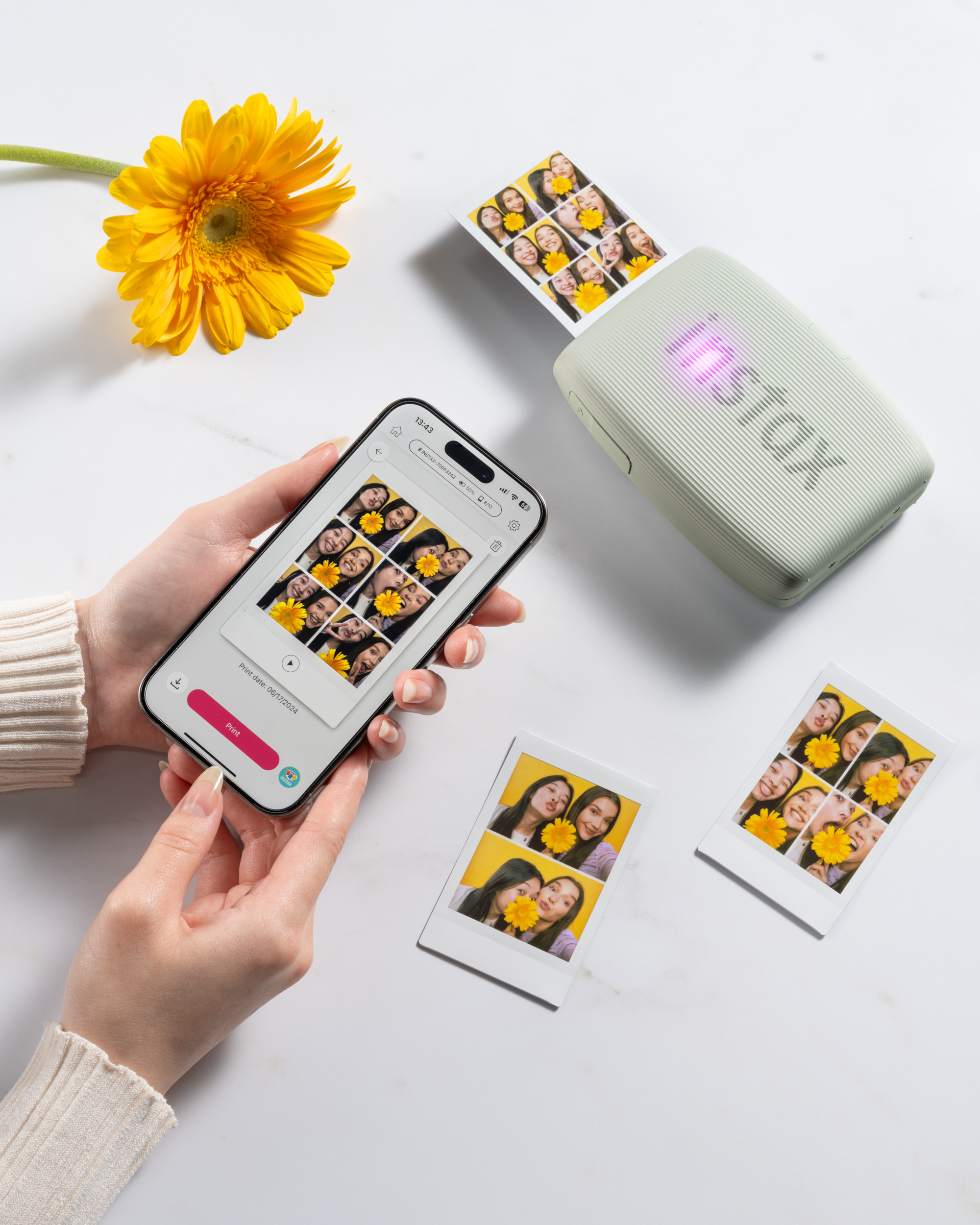 Een persoon print foto's vanaf een smartphone met een Instax-printer. Een gele bloem is zichtbaar.