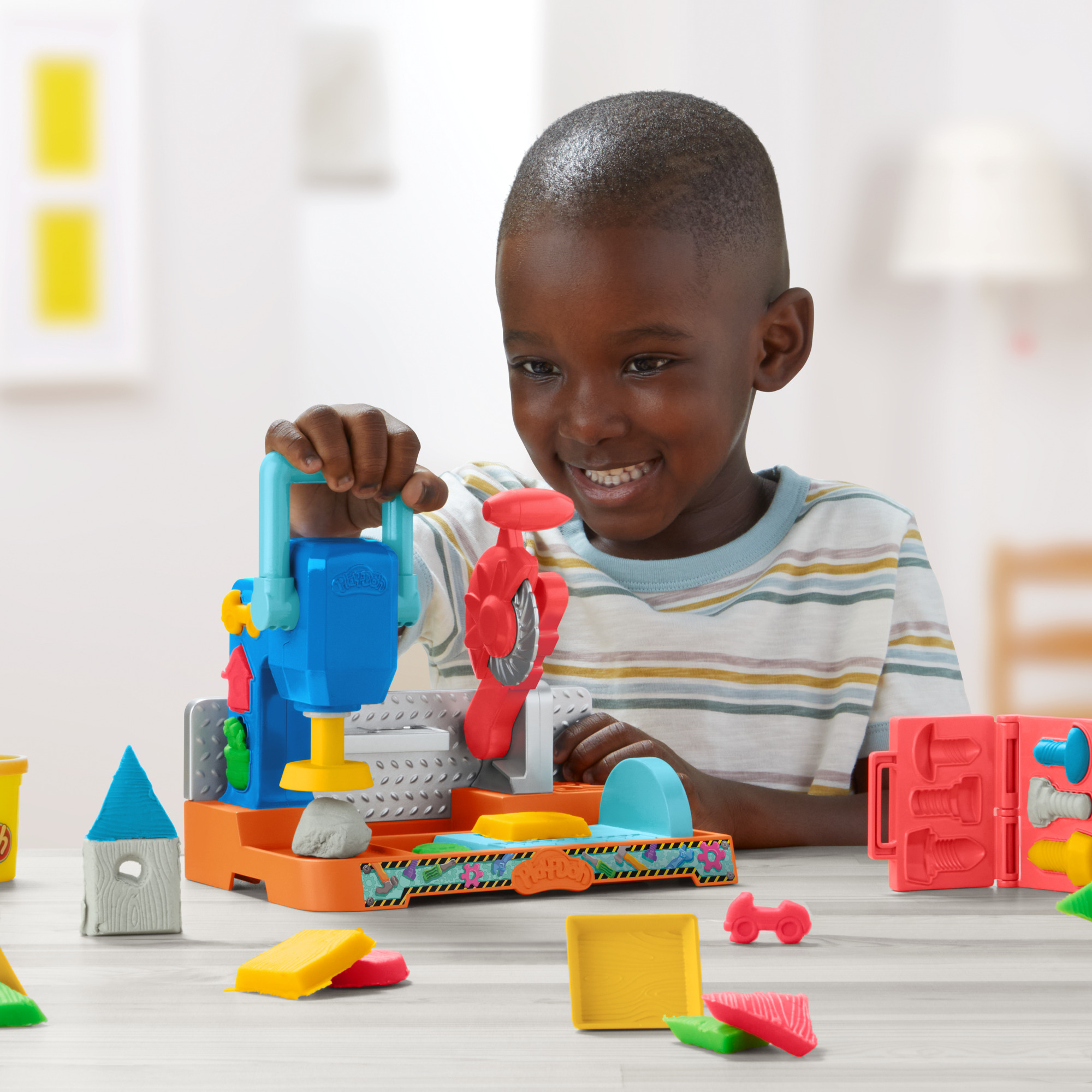 Un niño sonriente juega con herramientas de plastilina coloridas. Interactúa con un juego azul y naranja, con piezas de plastilina dispersas.