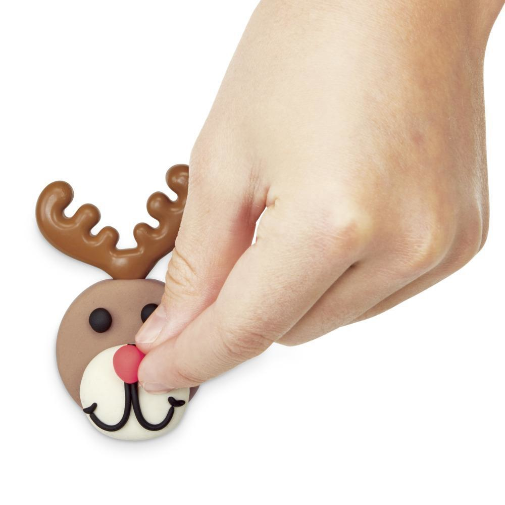 Dłoń dotyka glinianego renifera. Renifer ma brązowe rogi, jasnobrązową głowę, czarne oczy, czerwony nos i białe usta.