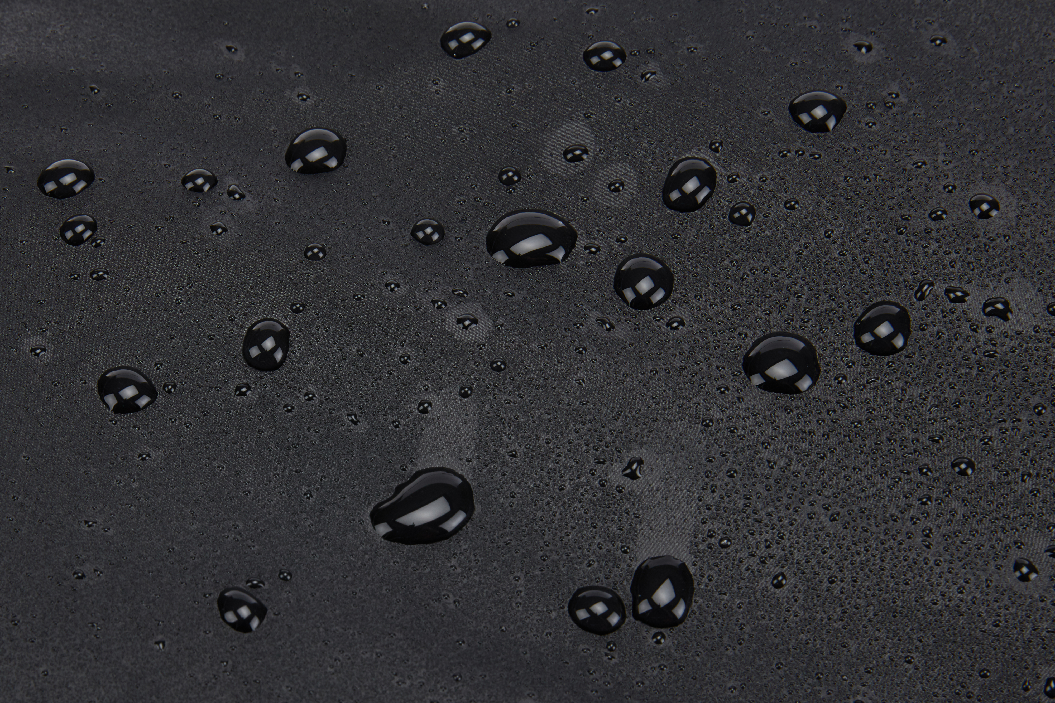 Zbliżenie czarnej powierzchni z rozproszonymi kroplami wody odbijającymi światło.