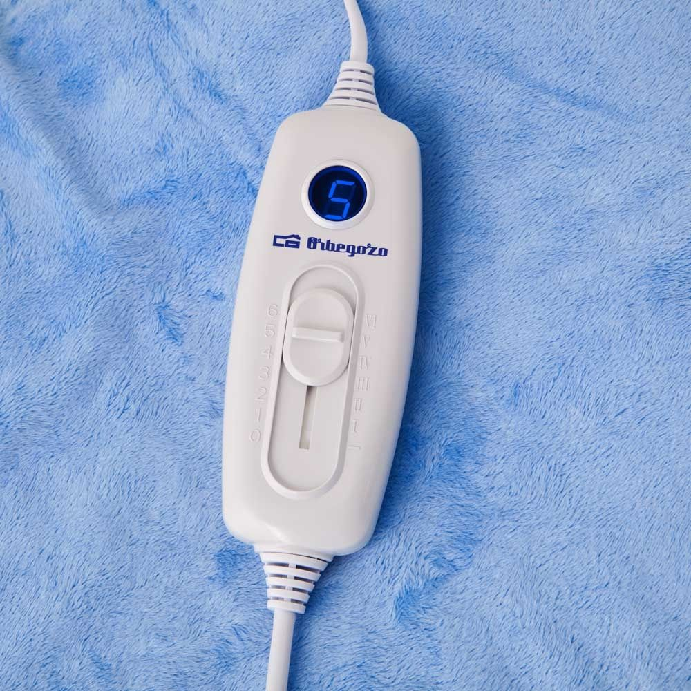 Biały kontroler koca elektrycznego z numerem 5. Na niebieskim, puszystym kocu.