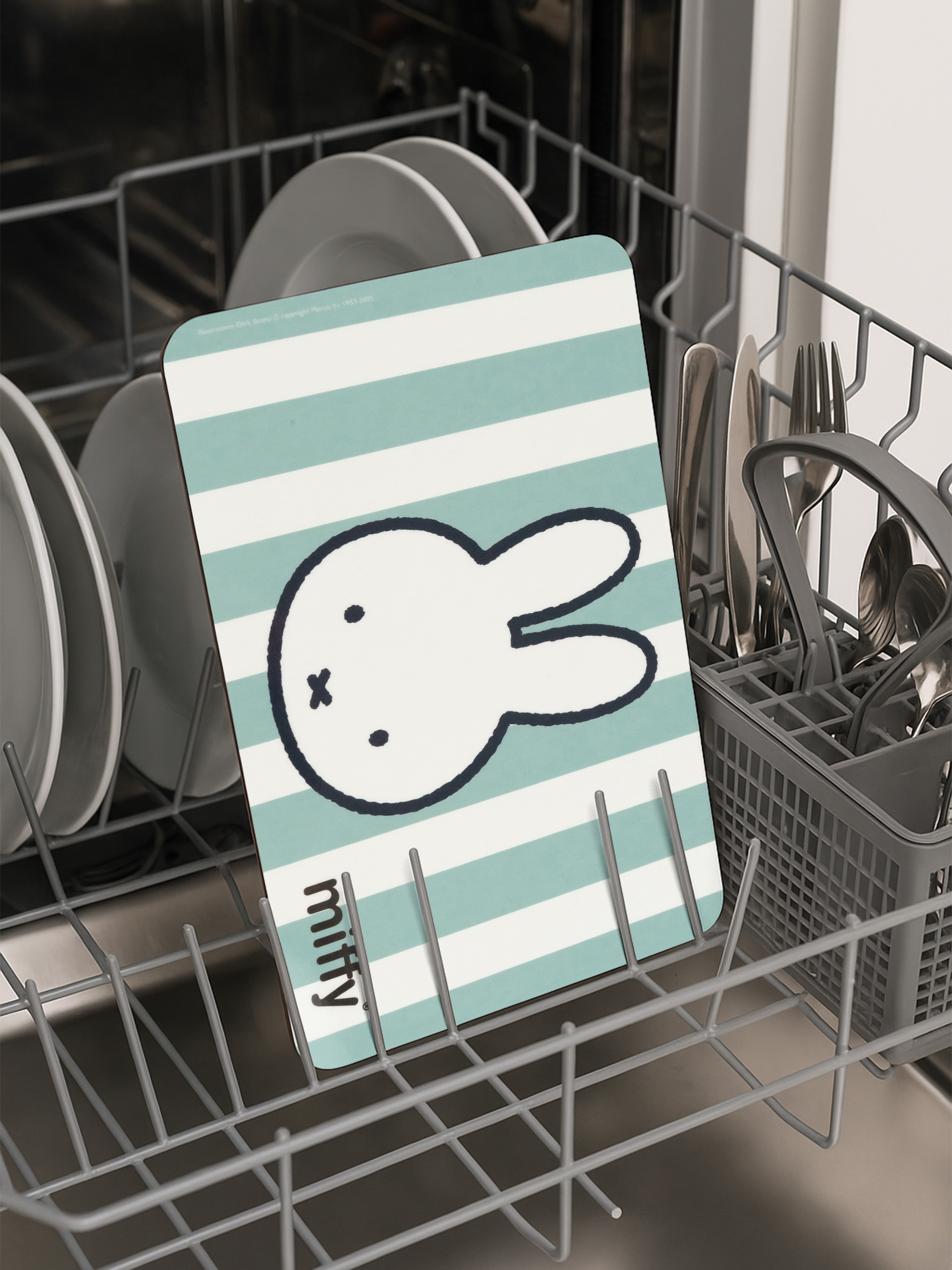 Geschirrspüler mit Tellern und einem Miffy-Schneidebrett. Das Brett hat einen gestreiften Hintergrund und ein Miffy-Gesicht.