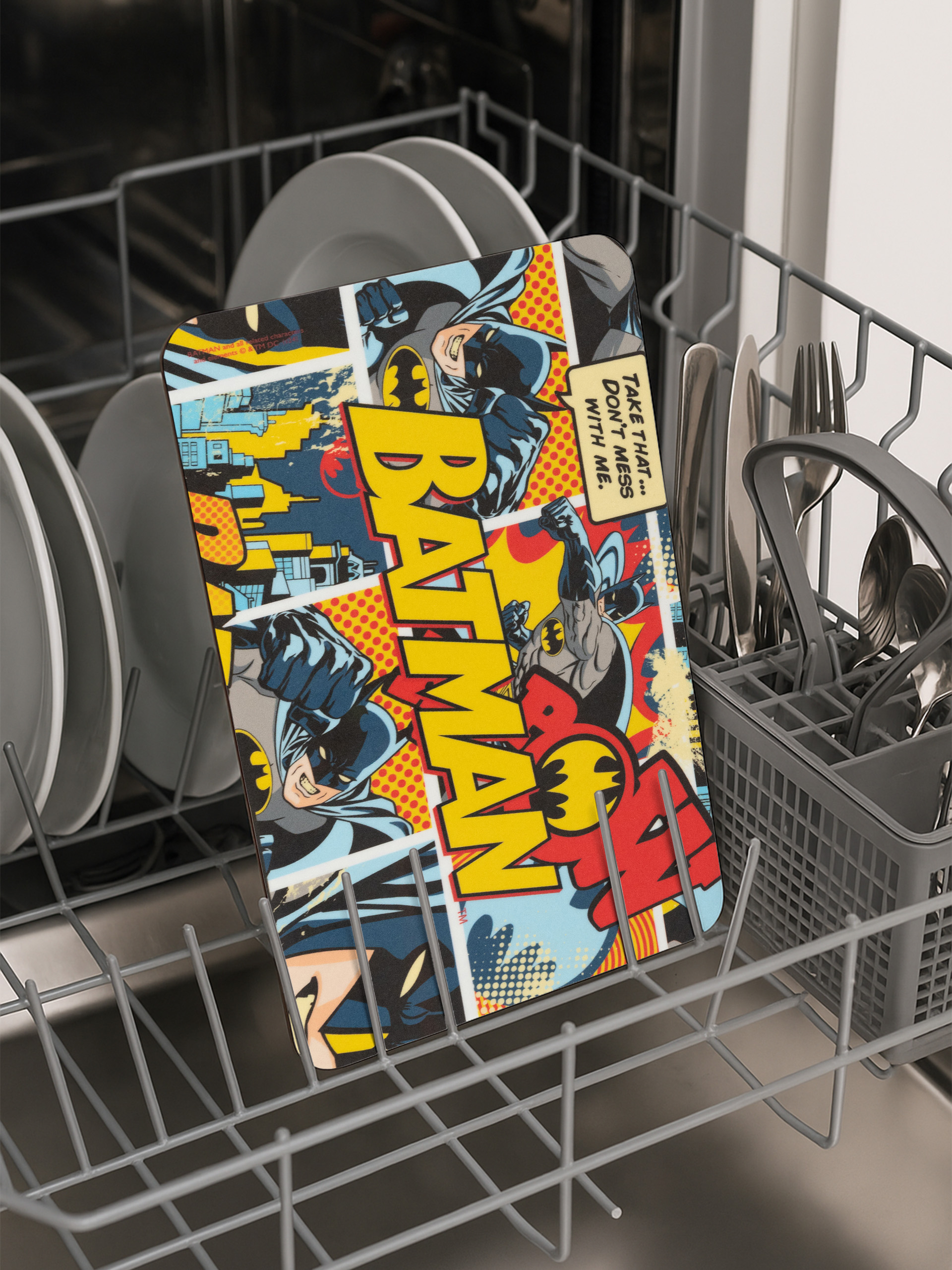 Batman-Schneidebrett in einer Spülmaschine. Comic-Stil mit Batman-Bildern, gelben und roten Farben.