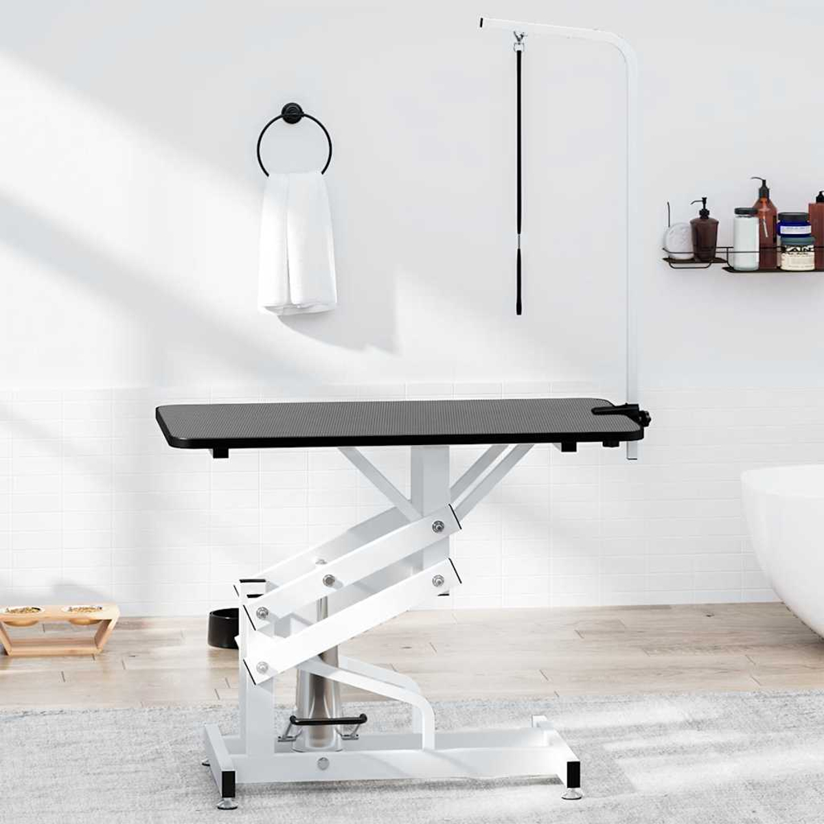 Ein weiß-schwarzer Pflegetisch. An einer weißen Wand befinden sich ein Handtuchring, ein Pflegearm und ein Regal mit Produkten.