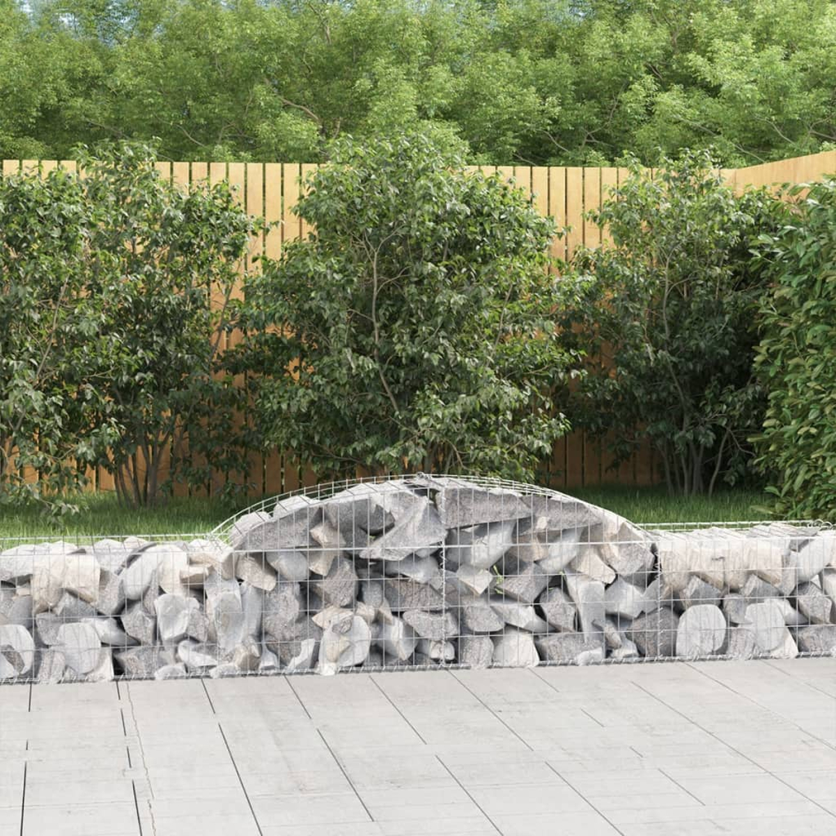 Eine Gartenszene. Im Vordergrund eine Steinmauer. Dahinter ein Holzzaun und grüne Büsche und Bäume.