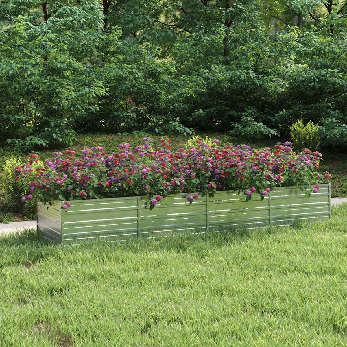 Ein Metallpflanzkasten mit leuchtenden Blumen in Rot- und Lilatönen, vor dem Hintergrund grüner Bäume und Gras.