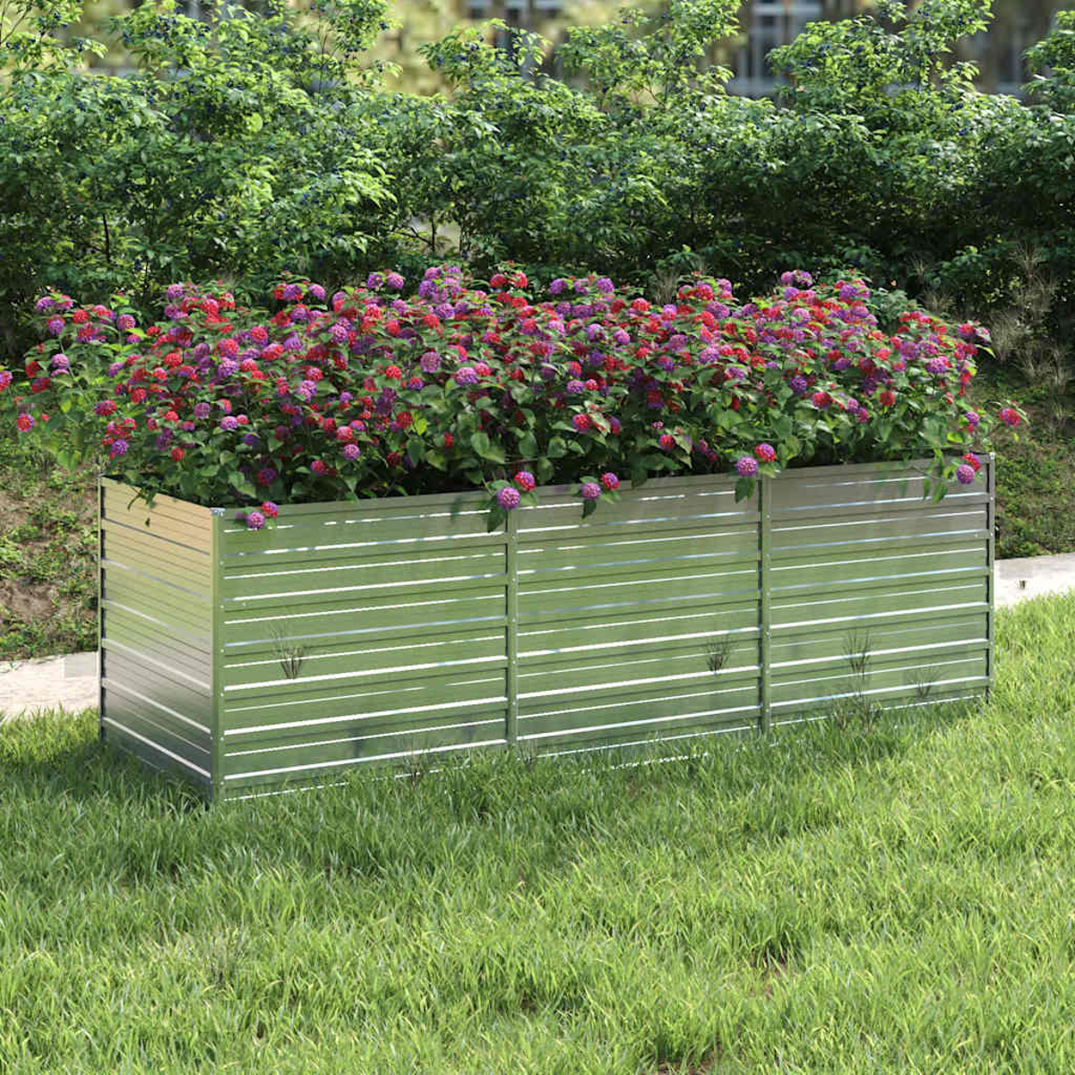 Metallpflanzkasten mit roten und lila Blumen. Grüne Büsche bilden den Hintergrund, auf einem Rasen.