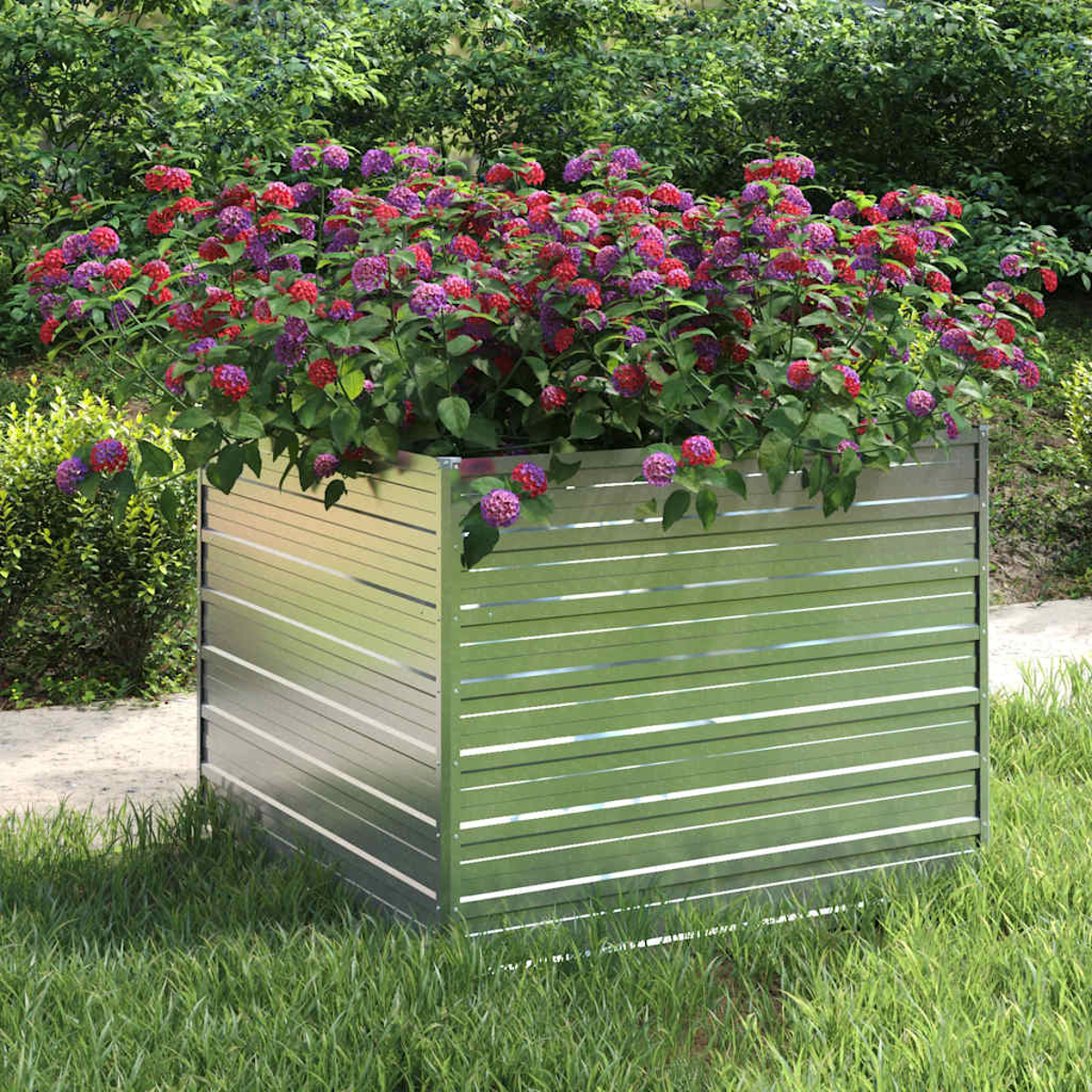 Eine Metallpflanzkasten mit roten und lila Blumen. Es steht auf Gras, im Hintergrund Grün und Büsche.
