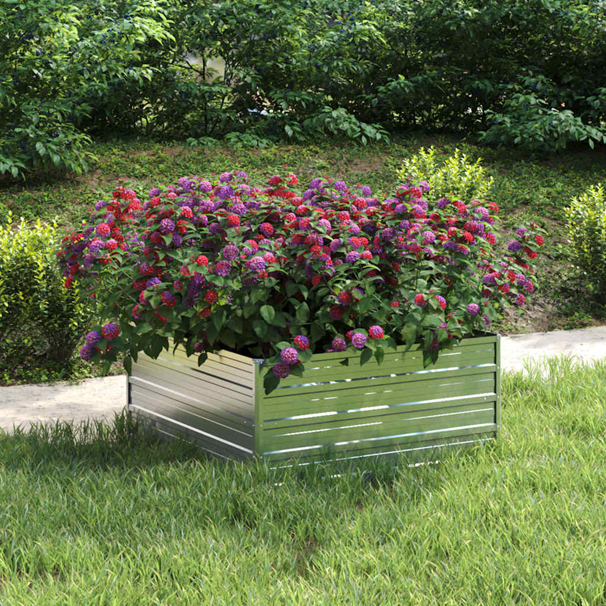 Eine Metallpflanzkasten mit roten und lila Blumen. Es steht auf Gras, im Hintergrund Büsche und Bäume.