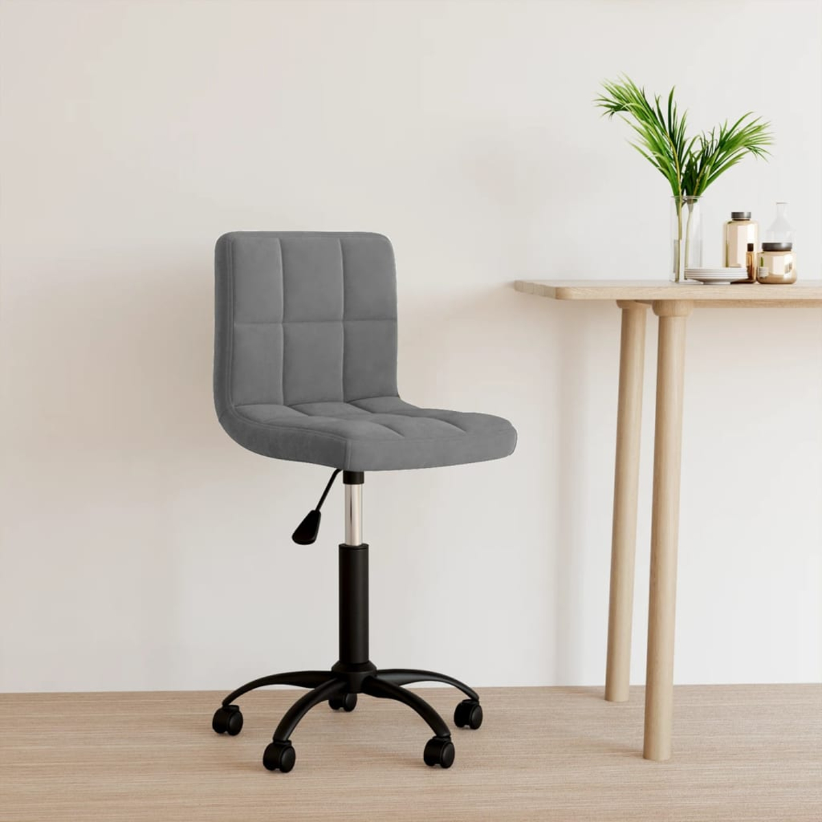 Ein grauer Bürostuhl mit schwarzem Gestell und Rollen steht neben einem Holztisch mit Dekorationen. Auf dem Tisch steht eine Pflanze.