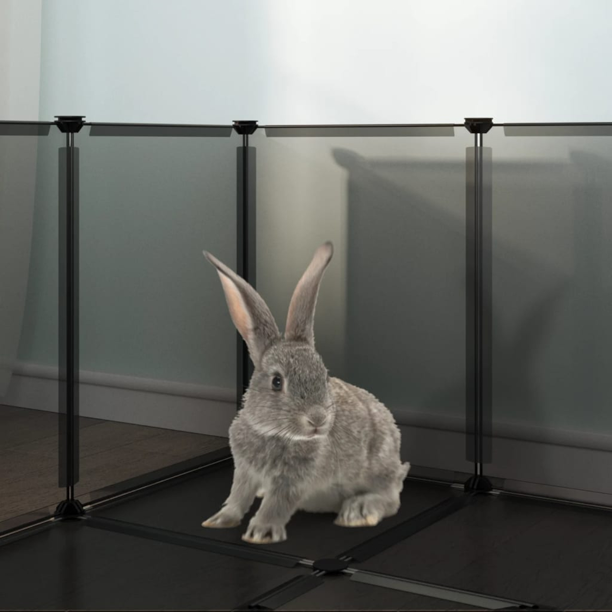Ein graues Kaninchen sitzt in einem schwarzen Gehege. Das Gehege steht vor einer hellgrünen Wand. Das Kaninchen hat lange Ohren und einen flauschigen Körper.