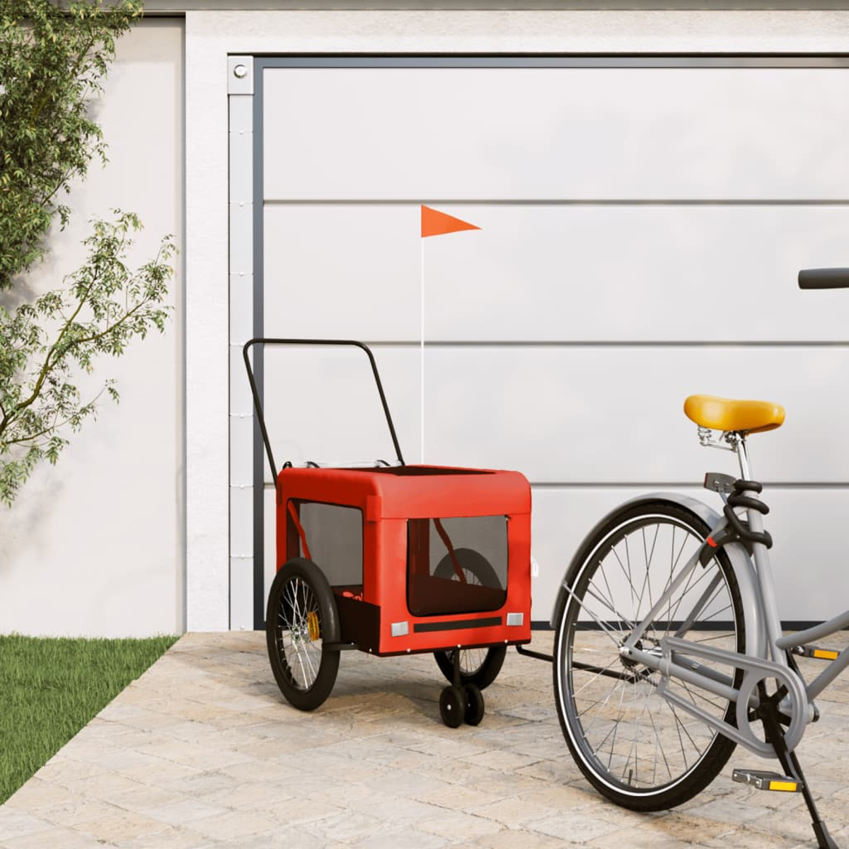 Ein roter Tieranhänger ist mit einem grauen Fahrrad verbunden. Eine kleine orangefarbene Fahne ist an der Garagentür befestigt.