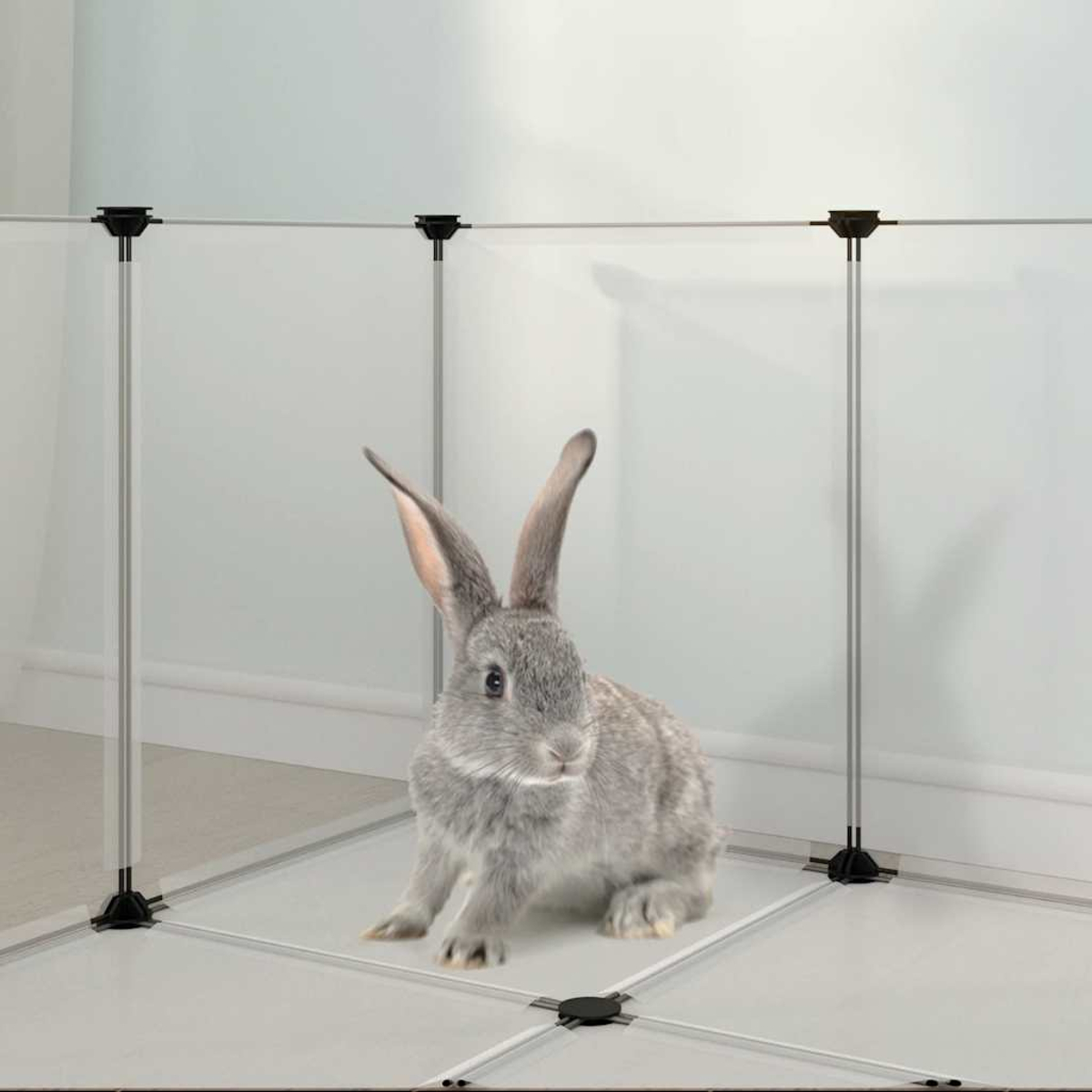 Ein graues Kaninchen sitzt in einem weißen Gehege. Das Gehege hat silberne Stangen und schwarze Verbinder. Weiße Wand im Hintergrund.
