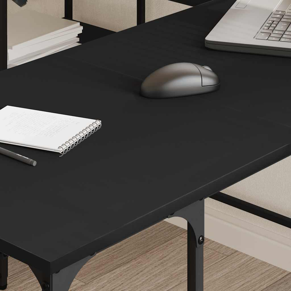 Ein schwarzer Schreibtisch mit Laptop, Maus, Notizblock und Stift. Der Schreibtisch steht auf einem Holzboden.