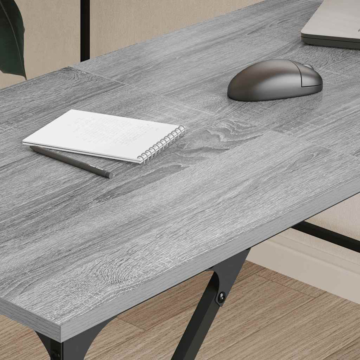 Grauer Holzschreibtisch mit Notizblock, Bleistift und Computermaus. Schwarze Metallbeine stützen den Tisch. Der Hintergrund ist eine Wand.