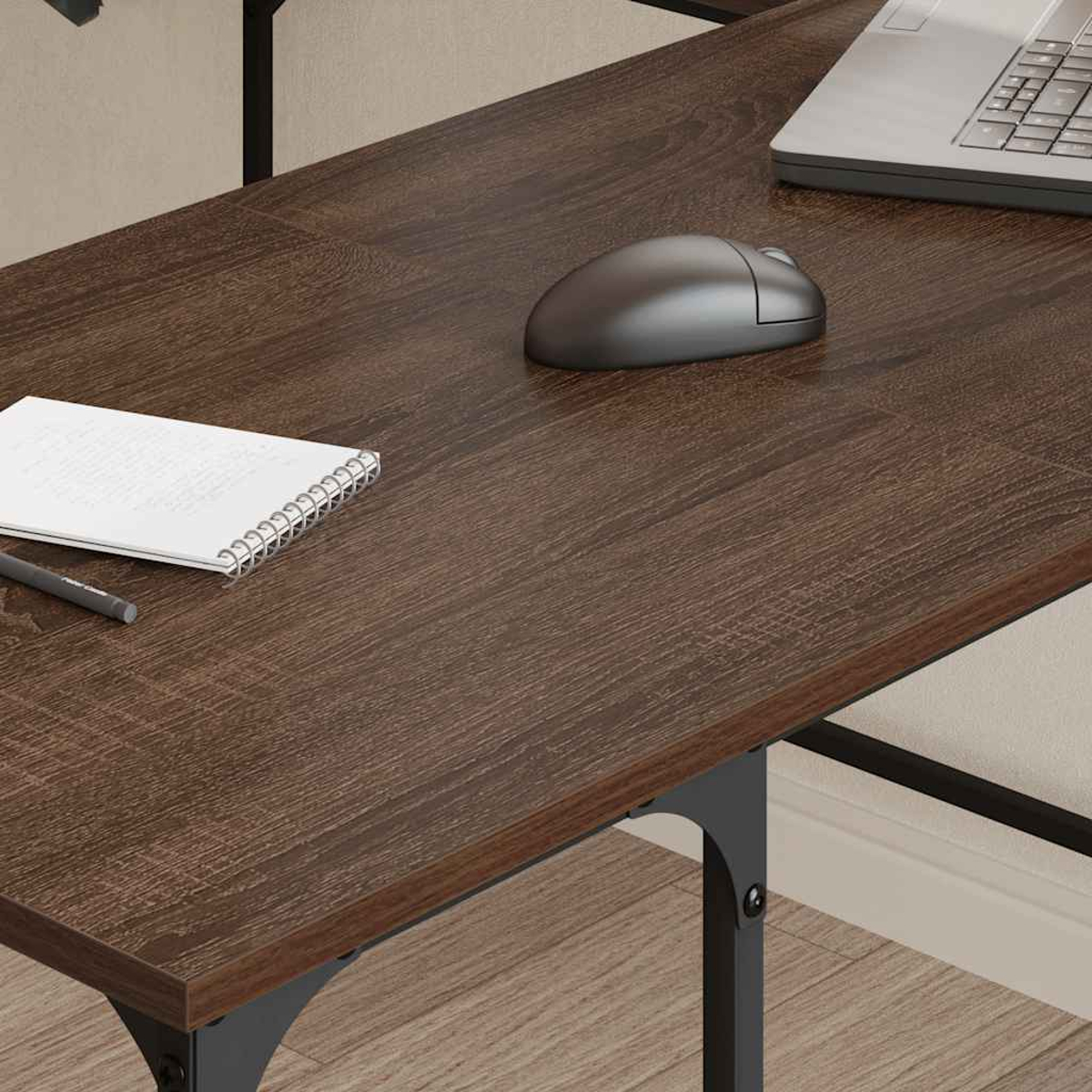 Ein dunkler Holzschreibtisch mit Laptop, Maus, Notizblock und Stift. Der Schreibtisch hat schwarze Metallbeine.