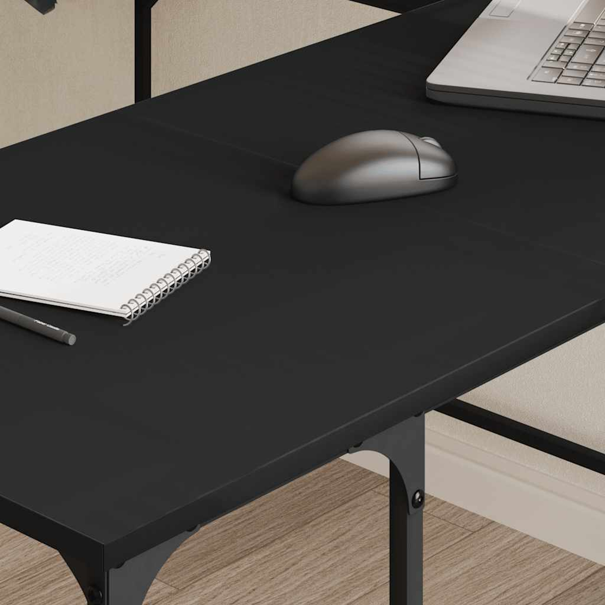 Schwarzer Schreibtisch mit Laptop, Maus, Notizblock und Stift. Holzboden und beige Wand im Hintergrund. Metallrahmen stützt den Tisch.