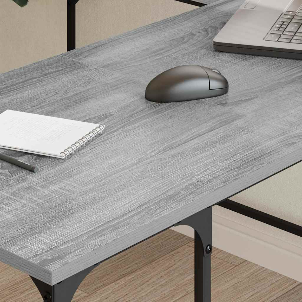Ein grauer Holzschreibtisch mit Laptop, Maus, Notizblock und Stift. Der Schreibtisch hat schwarze Metallbeine.
