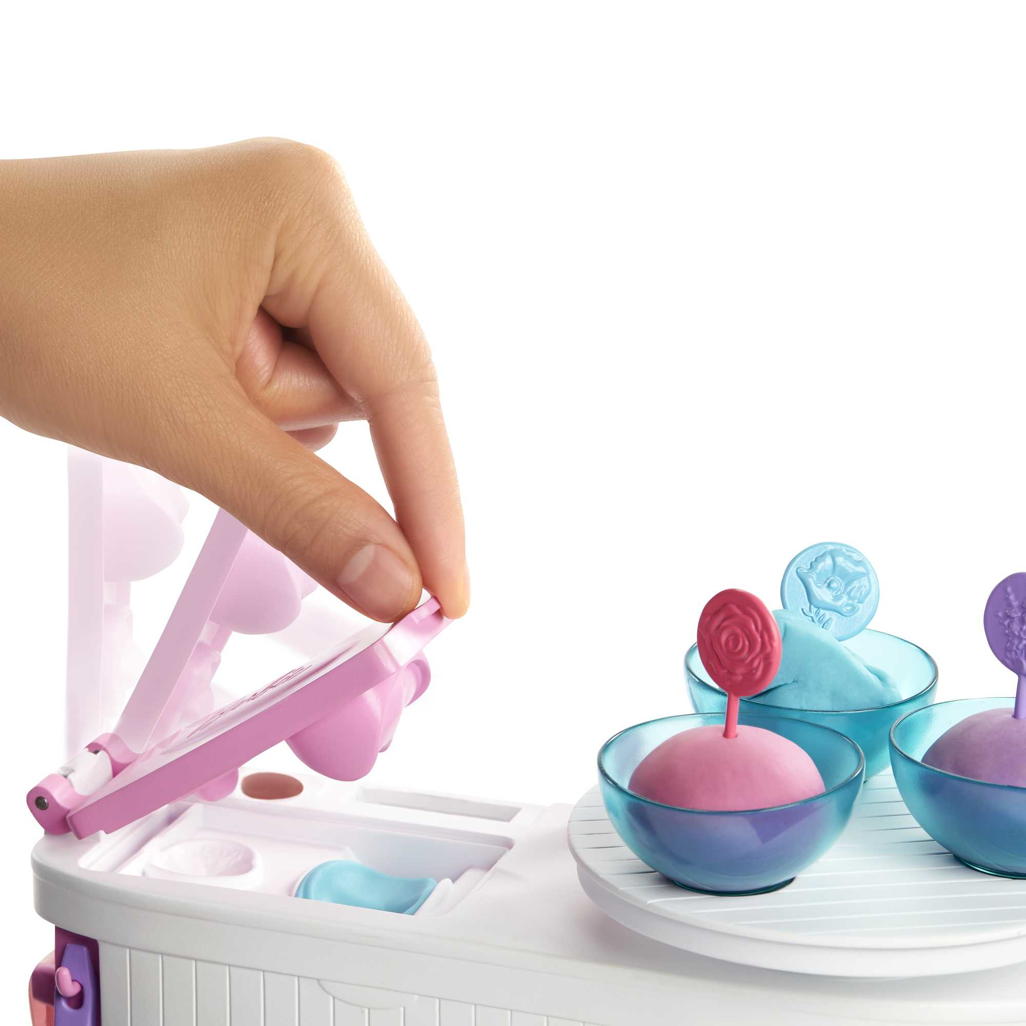 Ręka otwiera zabawkę. Miski z kolorową plasteliną i dekoracyjnymi patyczkami w tle.