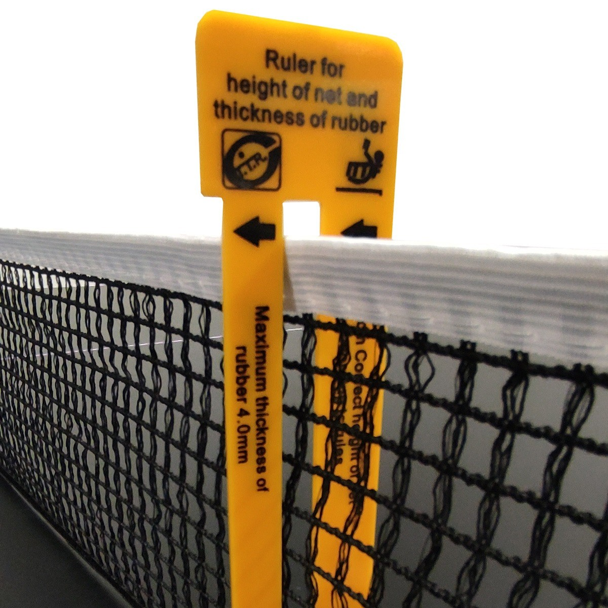 A yellow ruler measures a table tennis net. It specifies the maximum rubber thickness and the net's height. Black net is in the foreground.