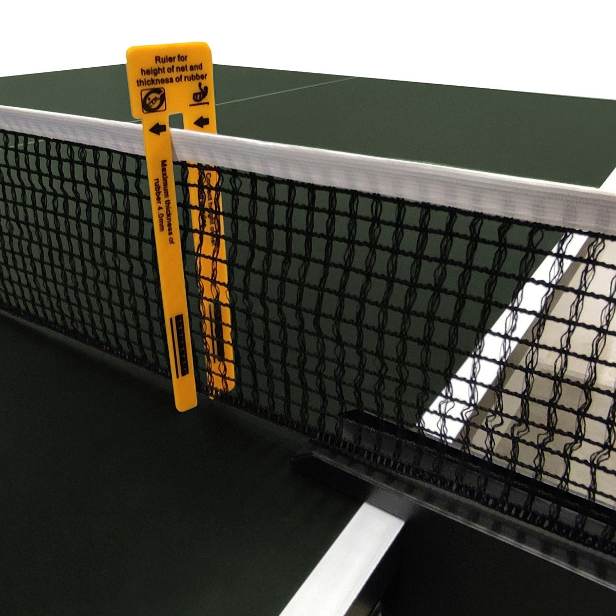 A ping pong net with an orange ruler measuring the net height and rubber thickness. The table is green.