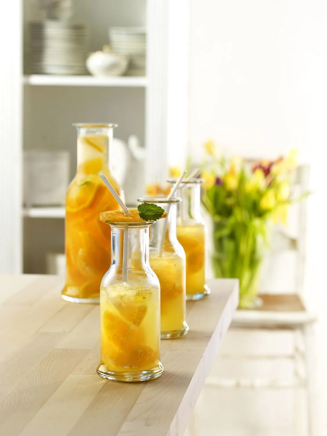 Bottles of orange drinks with straws and mint. A large bottle and three smaller ones are arranged on a wooden surface.