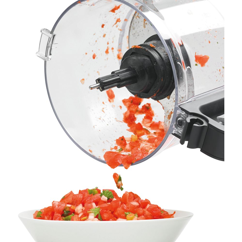 Un robot da cucina eroga pomodori ed erbe tritate in una ciotola bianca. Il robot è trasparente, mostrando residui all'interno.