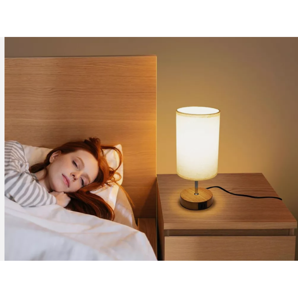 Eine Frau schläft im Bett, eine beleuchtete Lampe steht auf dem Nachttisch. Die Szene ist warm und einladend.