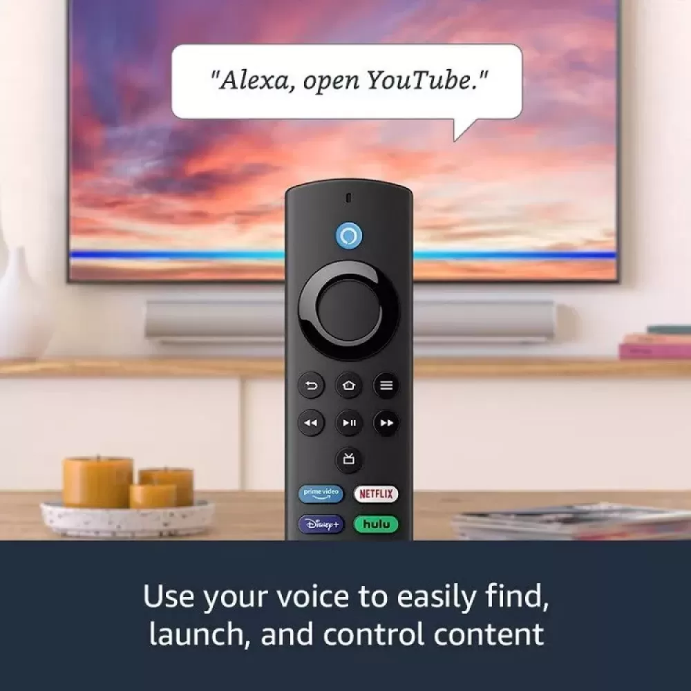 Schwarze Fernbedienung mit Alexa-Sprachbefehl-Blase. Fernseher im Hintergrund, Kerzen und Streaming-Dienst-Buttons sichtbar.