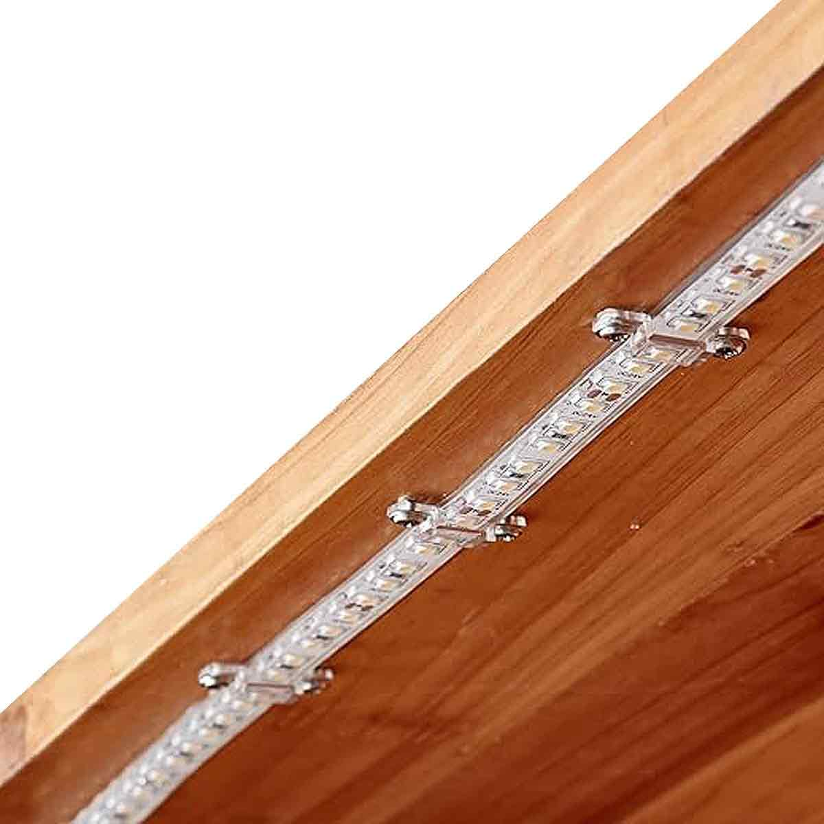 LED-Streifen auf Holz montiert. Silberclips befestigen den Streifen. Das Holz ist braun. Weißer Hintergrund.