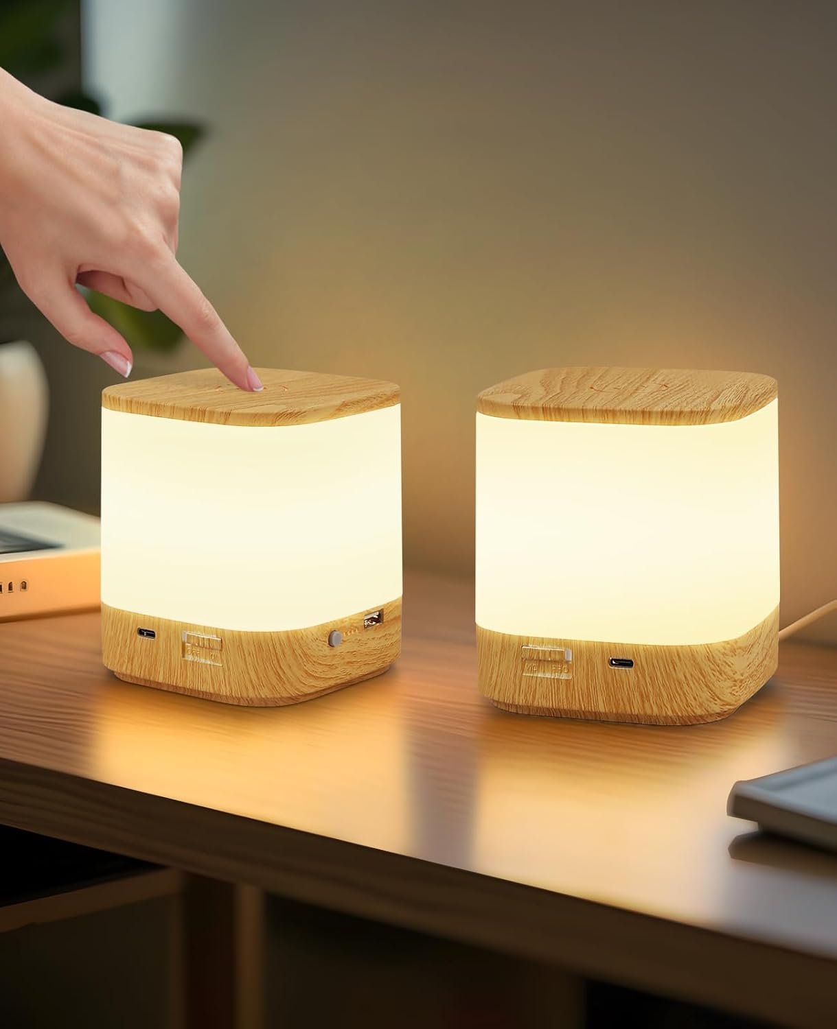 Una mano tocca una lampada di legno. Due lampade luminose con top in legno sono su una superficie di legno.
